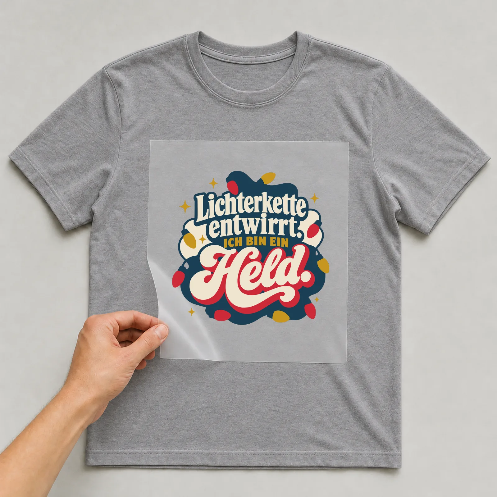 Bügelbild Lichterkette entwirrt. Ich bin ein Held. auf grauem T-Shirt, Folie wird aufgelegt