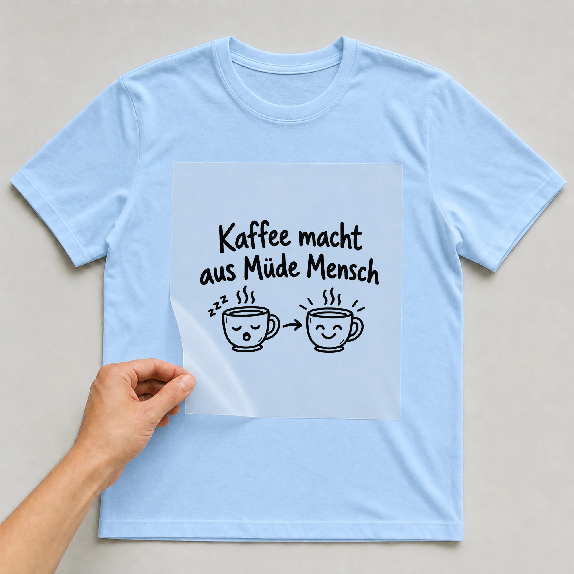 Bügelbild „Kaffee macht aus Müde Mensch“ auf babyblauem T-Shirt, Folie wird aufgelegt