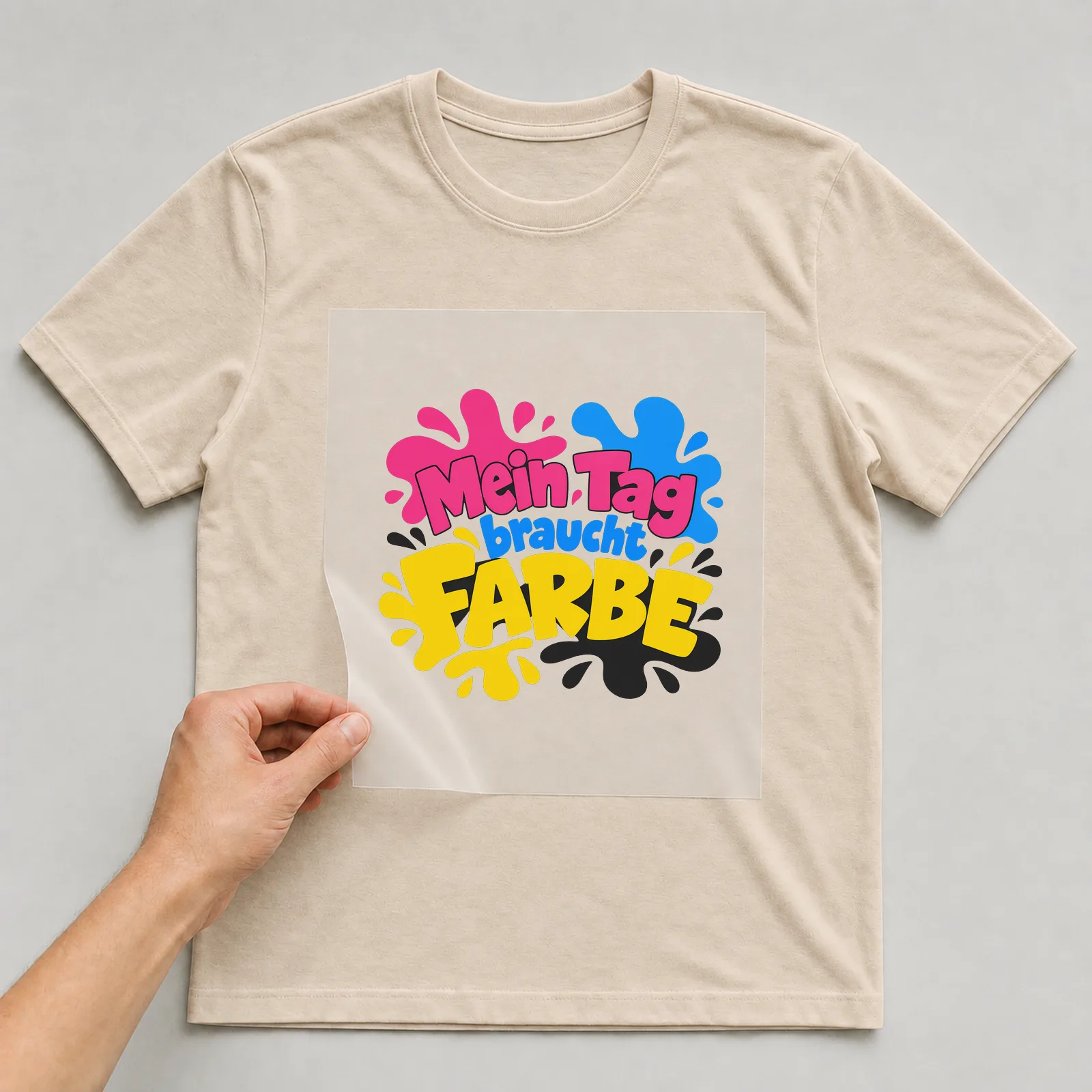 Bügelbild „Mein Tag braucht Farbe“ auf beigem T-Shirt, Folie wird aufgelegt