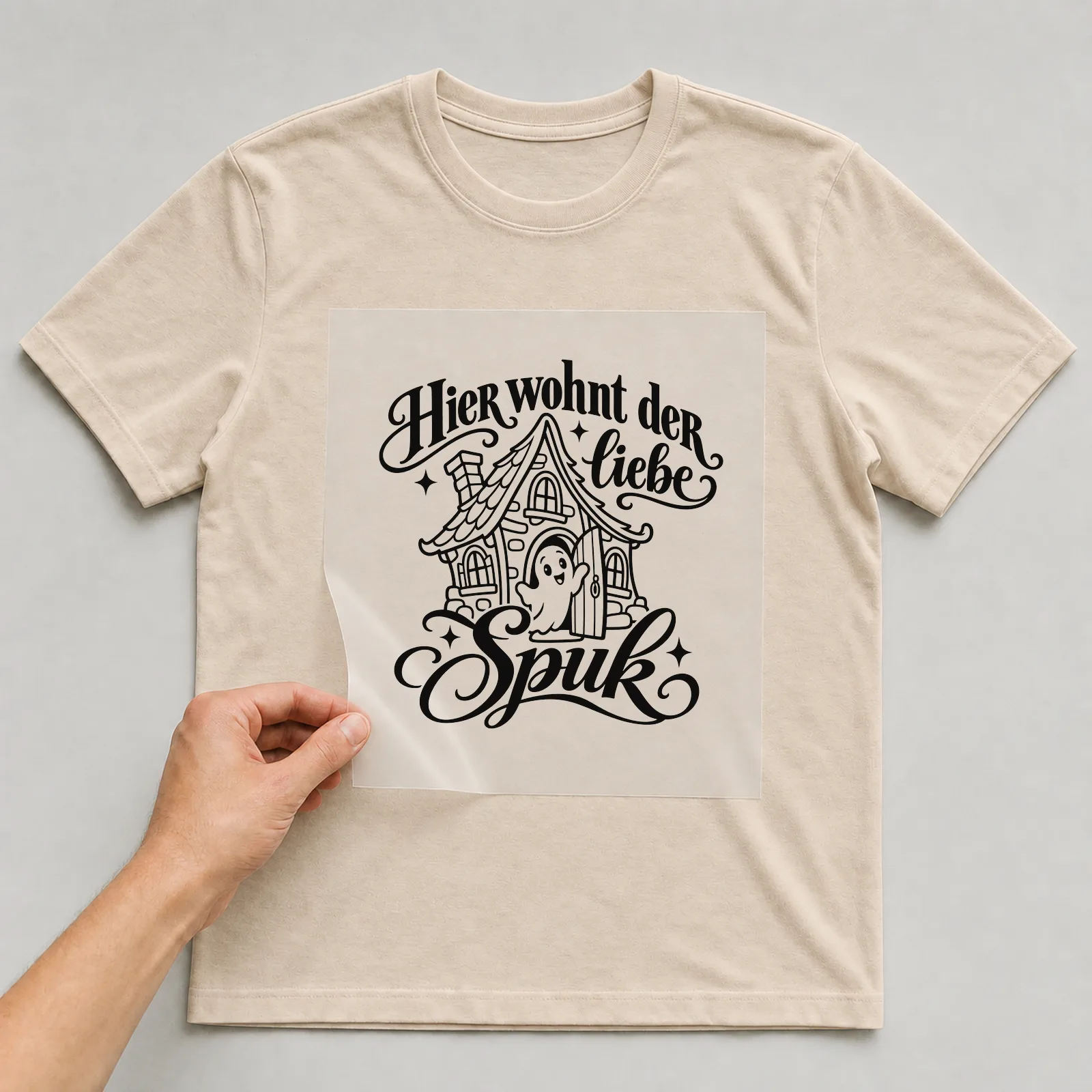 Bügelbild „Hier wohnt der liebe Spuk“ auf beigem T-Shirt, Folie wird aufgelegt