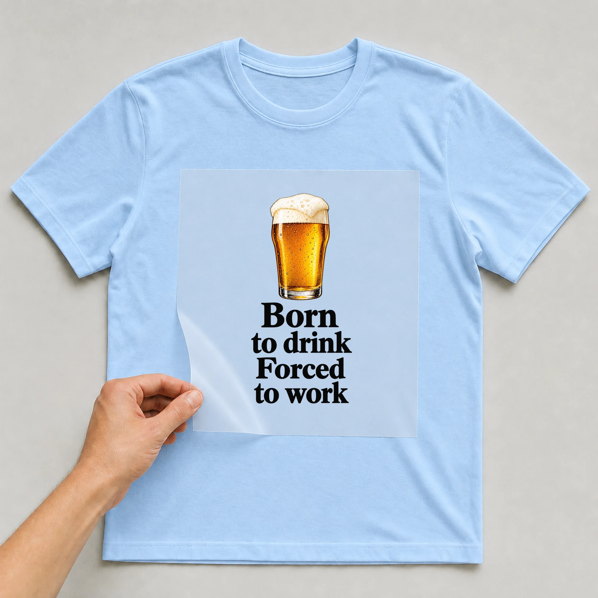 Bügelbild „Born to drink Forced to work“ auf babyblauem T-Shirt, Folie wird aufgelegt
