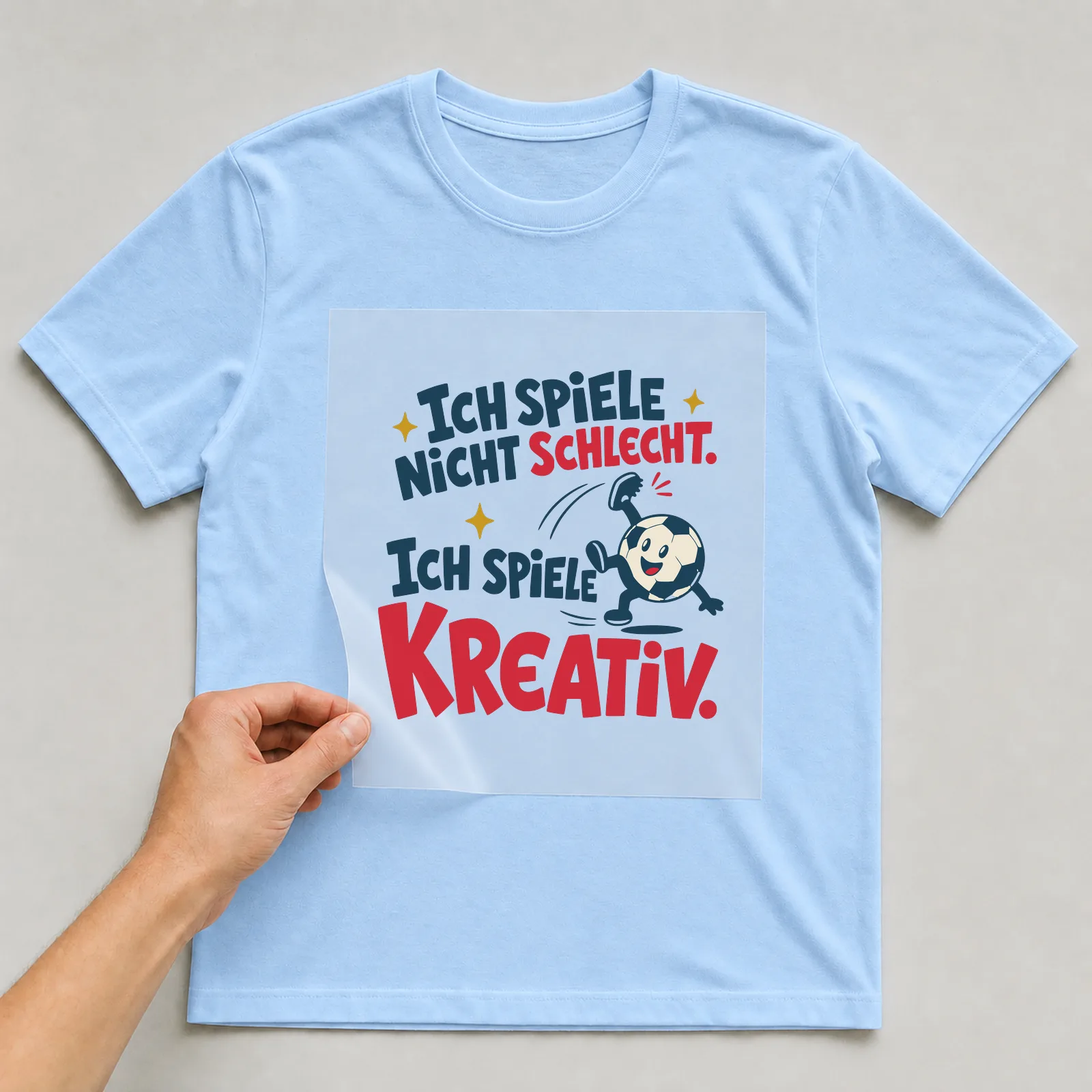 Bügelbild Ich spiele nicht schlecht. Ich spiele kreativ. auf hellblauem T-Shirt, Folie wird aufgelegt