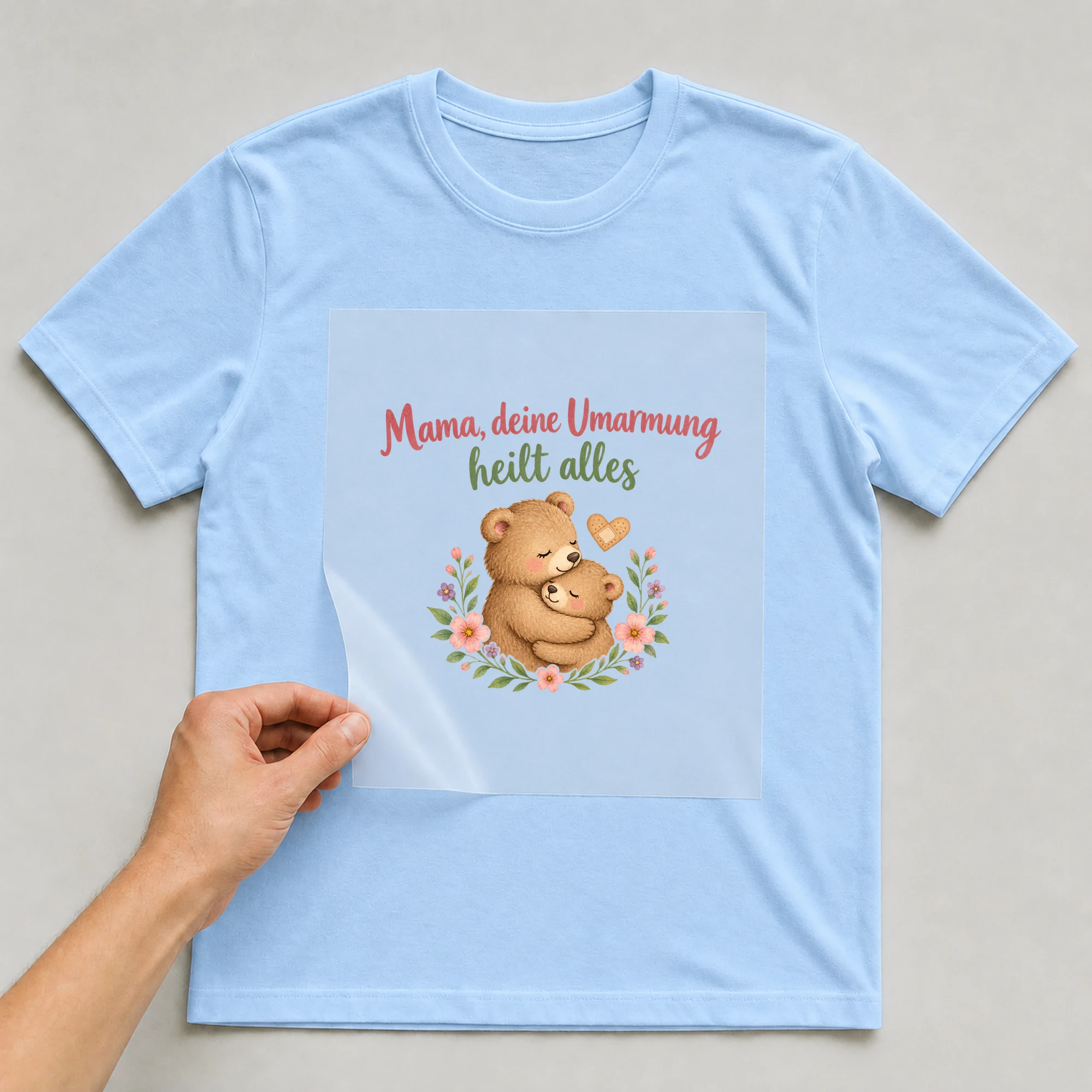 Bügelbild „Mama, deine Umarmung heilt alles“ auf babyblauem T-Shirt, Folie wird aufgelegt
