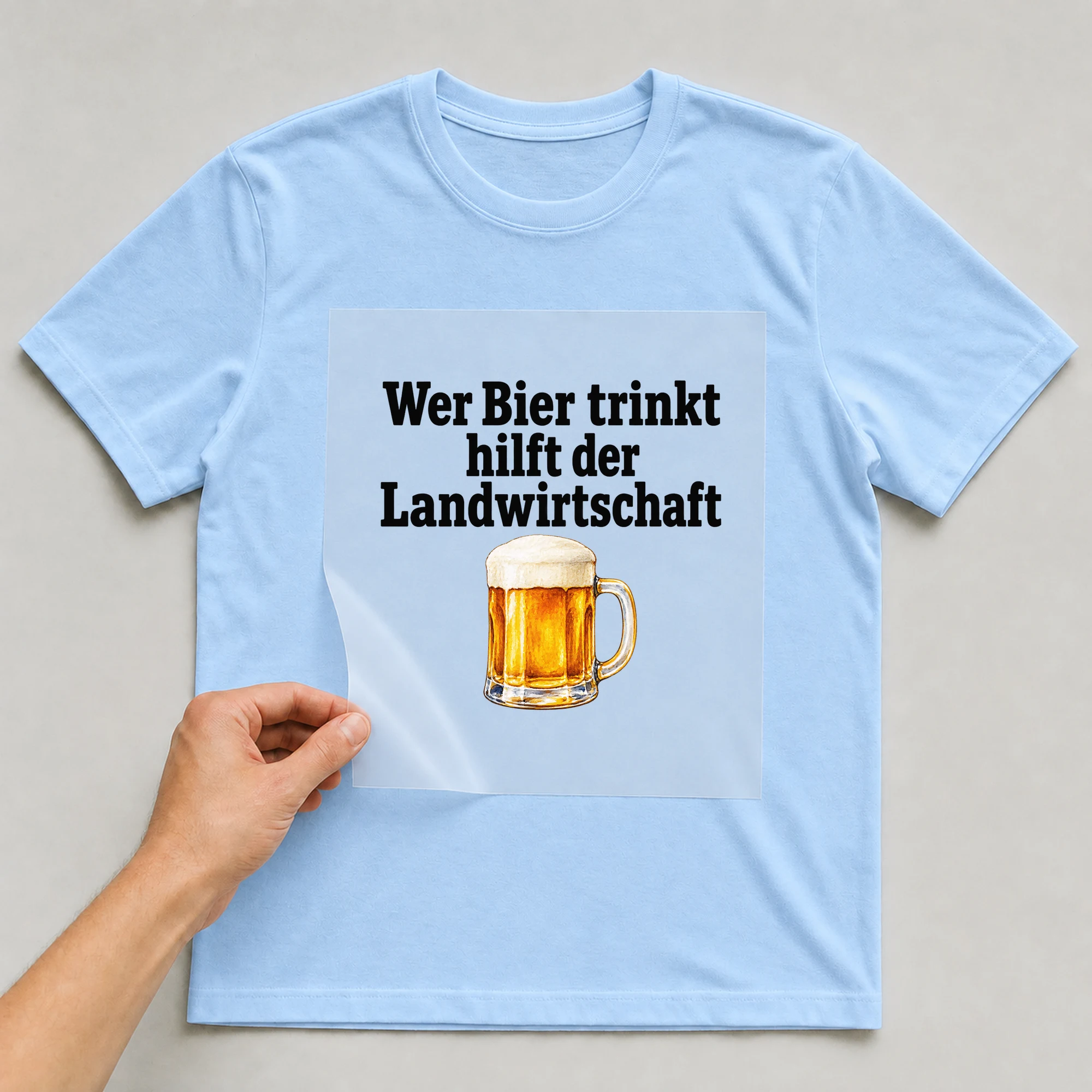 Bügelbild „Wer Bier trinkt hilft der Landwirtschaft“ auf babyblauem T-Shirt, Folie wird aufgelegt