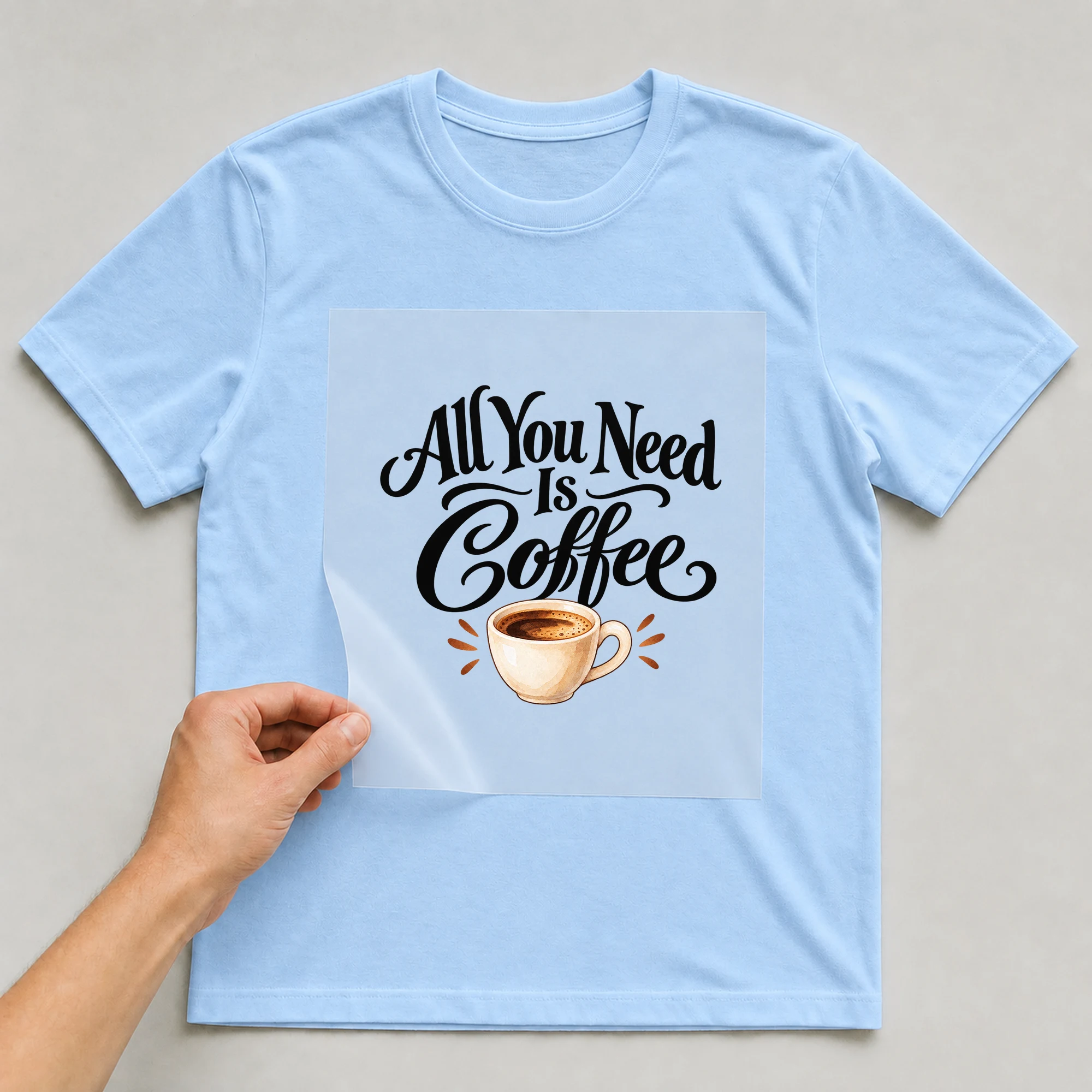 Bügelbild „All You Need Is Coffee“ auf babyblauem T-Shirt, Folie wird aufgelegt