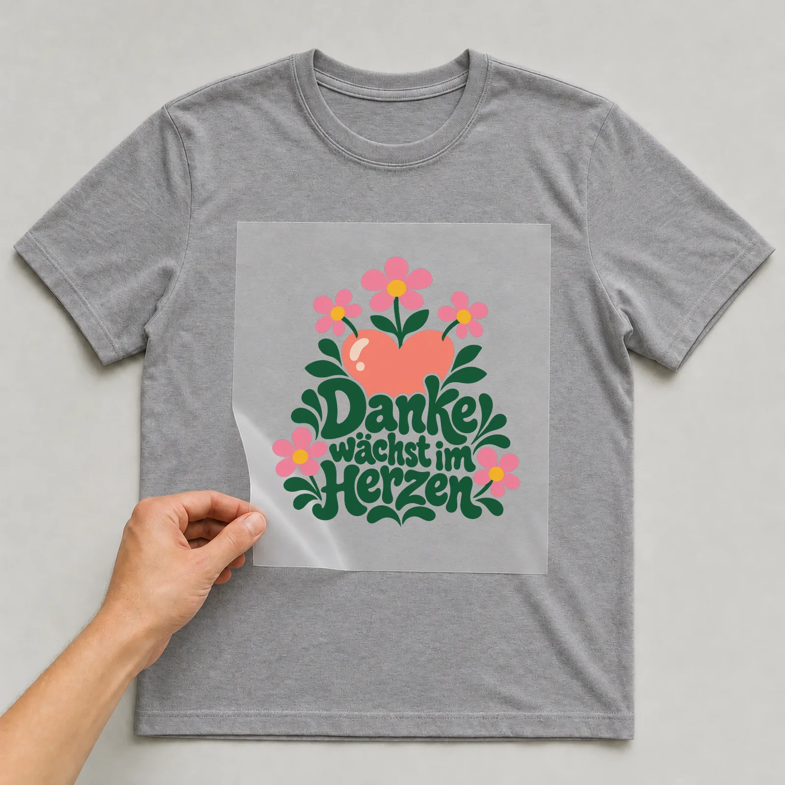 Bügelbild „Danke wächst im Herzen“ auf grauem T-Shirt, Folie wird aufgelegt