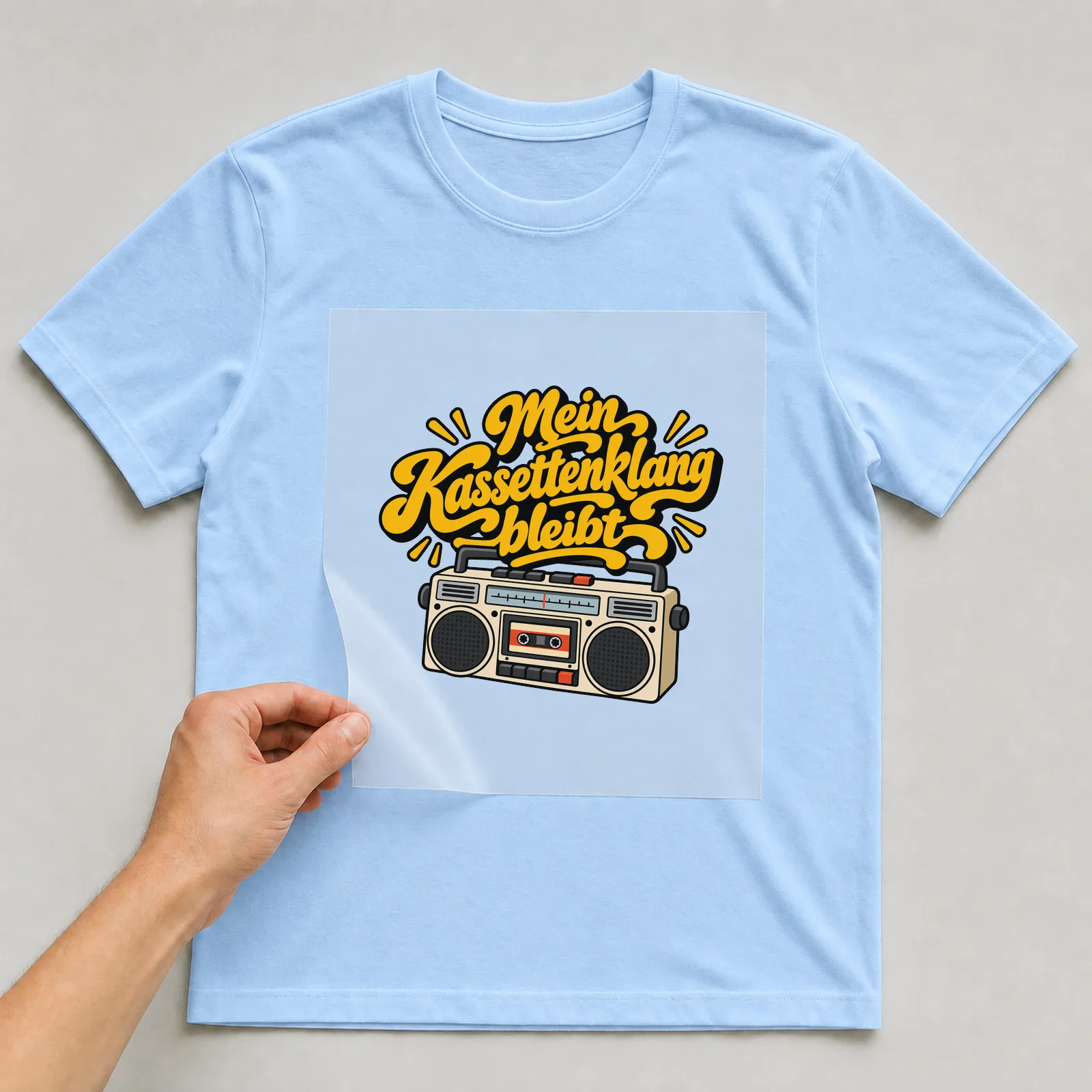 Bügelbild „Mein Kassettenklang bleibt“ auf hellblauem T-Shirt, Folie wird aufgelegt