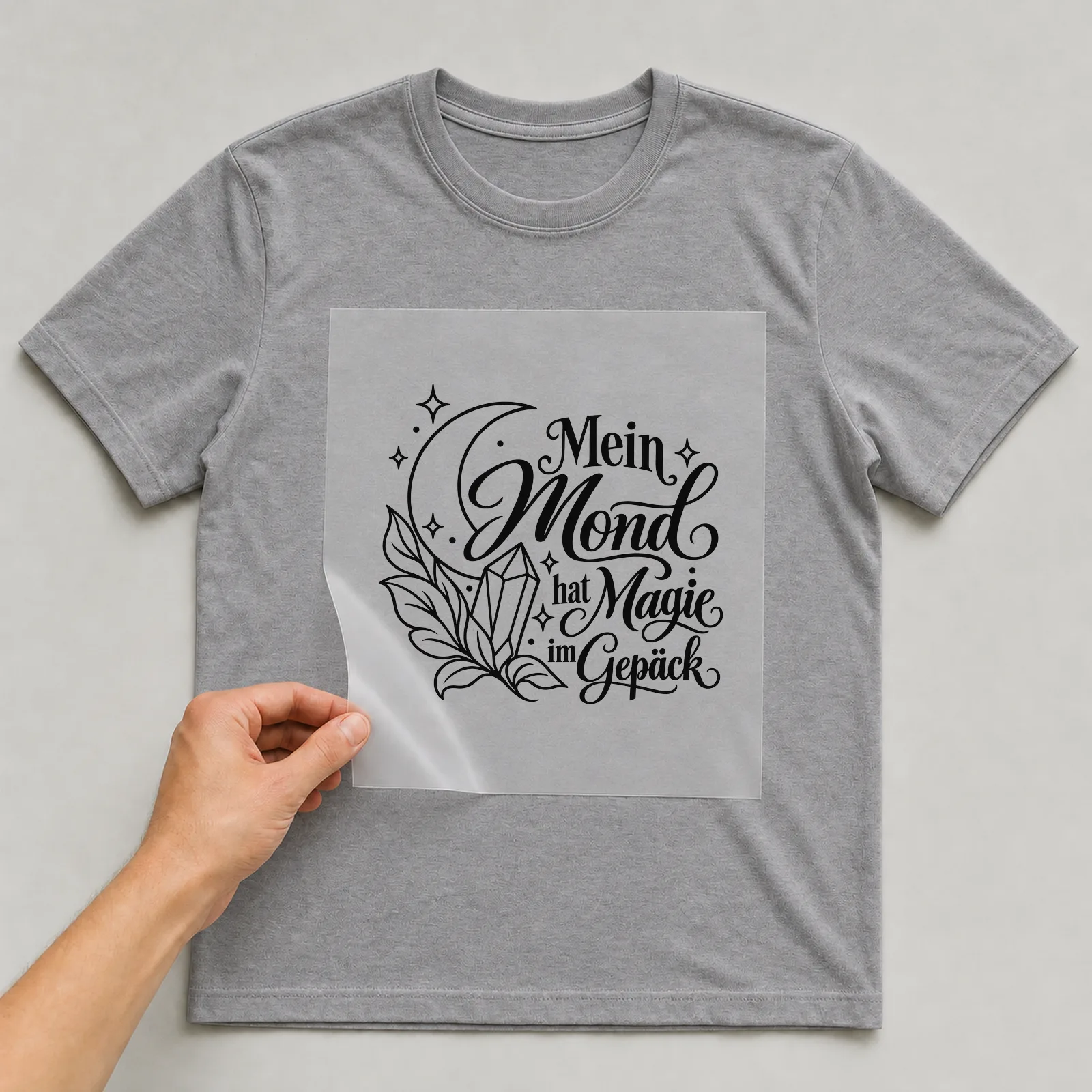 Bügelbild „Mein Mond hat Magie im Gepäck“ auf grauem T-Shirt, Folie wird aufgelegt