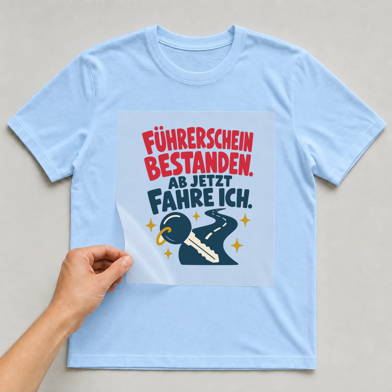Bügelbild Führerschein bestanden. Ab jetzt fahre ich. auf hellblauem T-Shirt, Folie wird aufgelegt