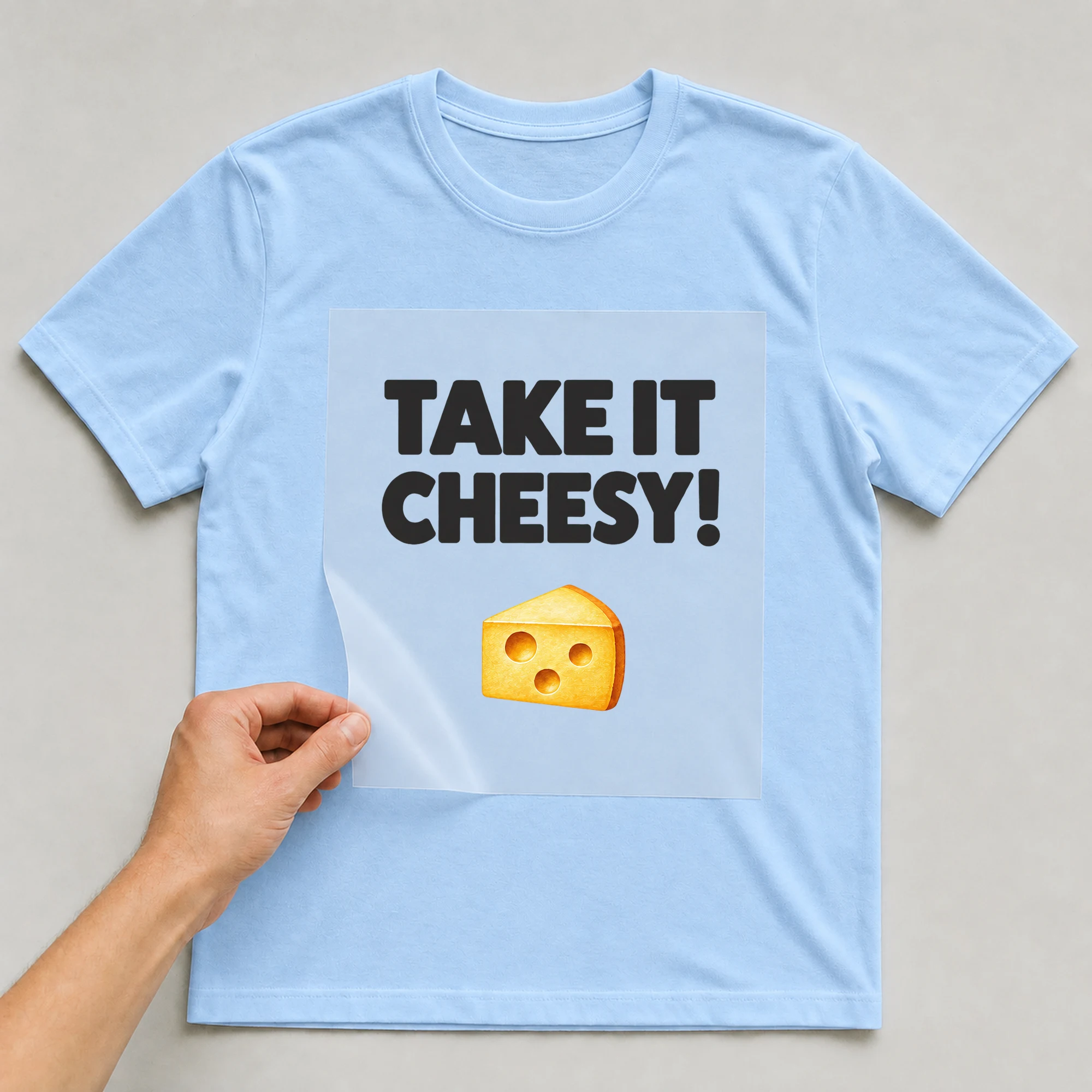 Bügelbild „TAKE IT CHEESY!“ auf babyblauem T-Shirt, Folie wird aufgelegt