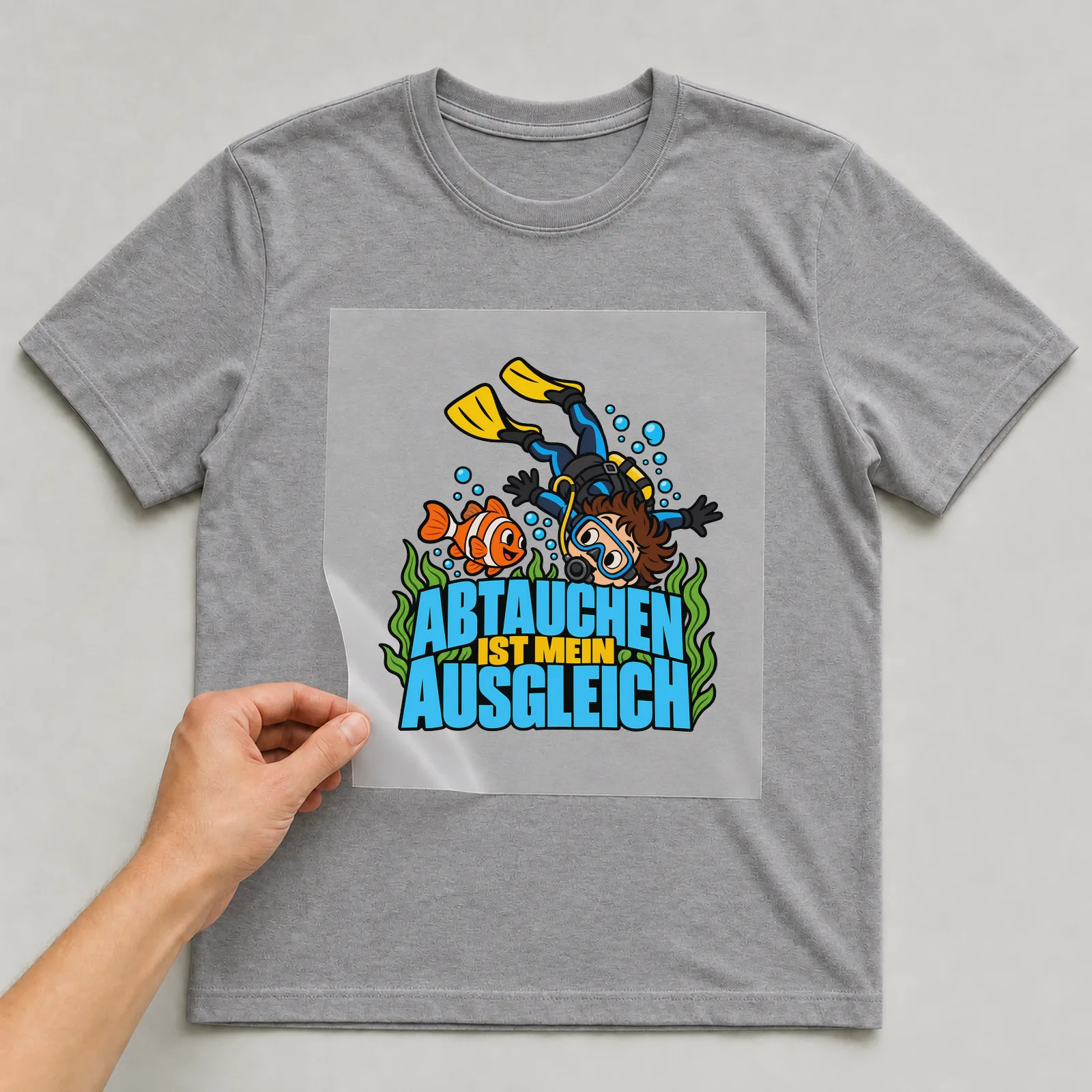Bügelbild „Abtauchen ist mein Ausgleich“ auf grauem T-Shirt, Folie wird aufgelegt