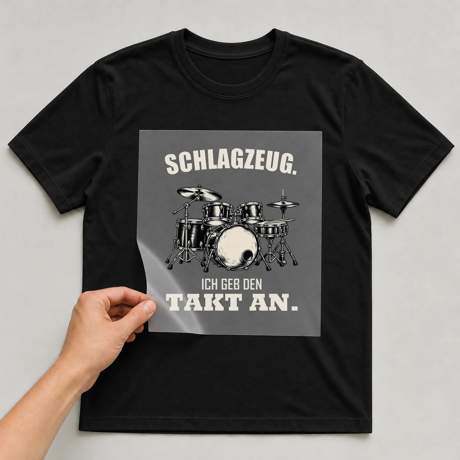 Bügelbild „Schlagzeug. Ich geb den Takt an.“ auf schwarzem T-Shirt, Folie wird aufgelegt