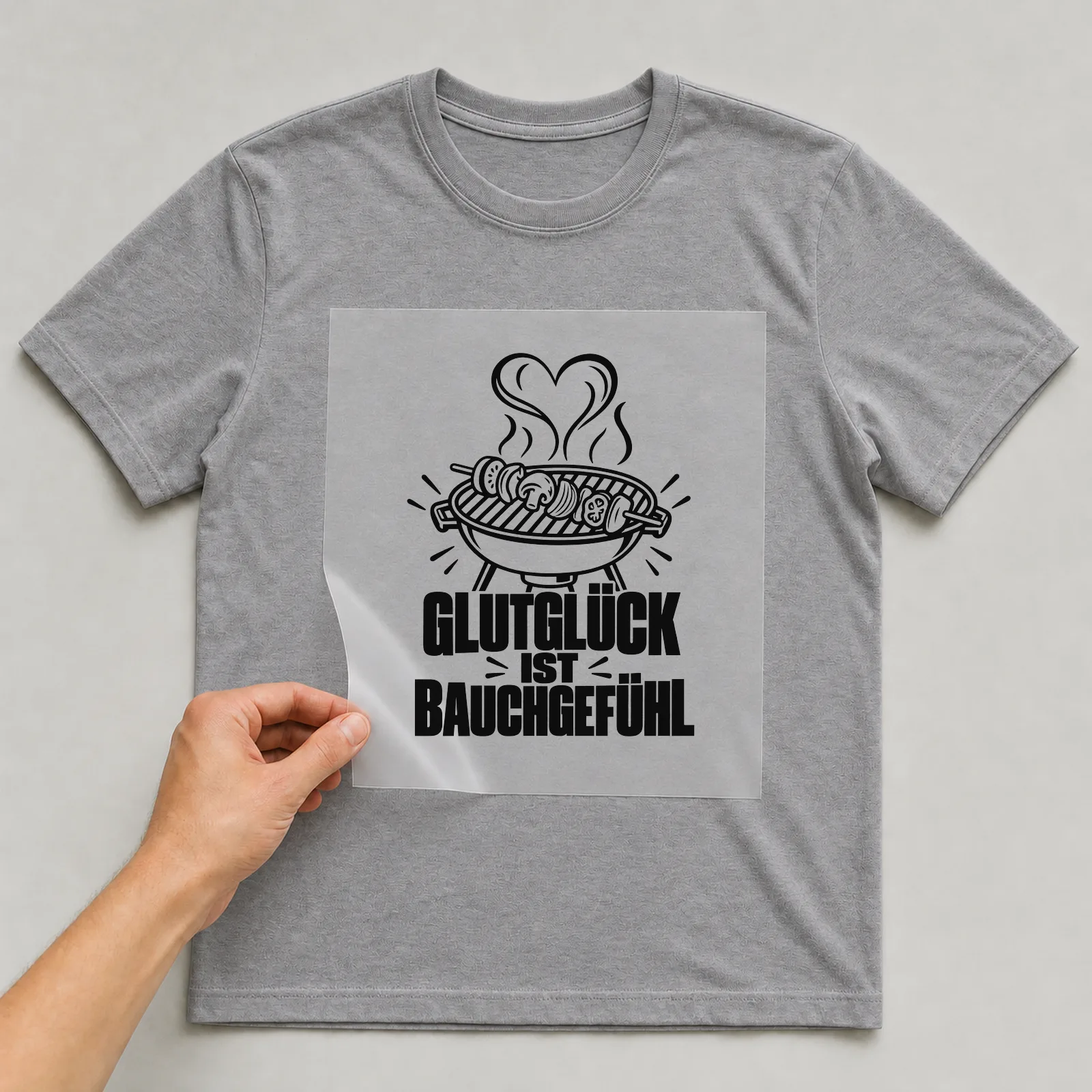 Bügelbild „Glutglück ist Bauchgefühl“ auf grauem T-Shirt, Folie wird aufgelegt