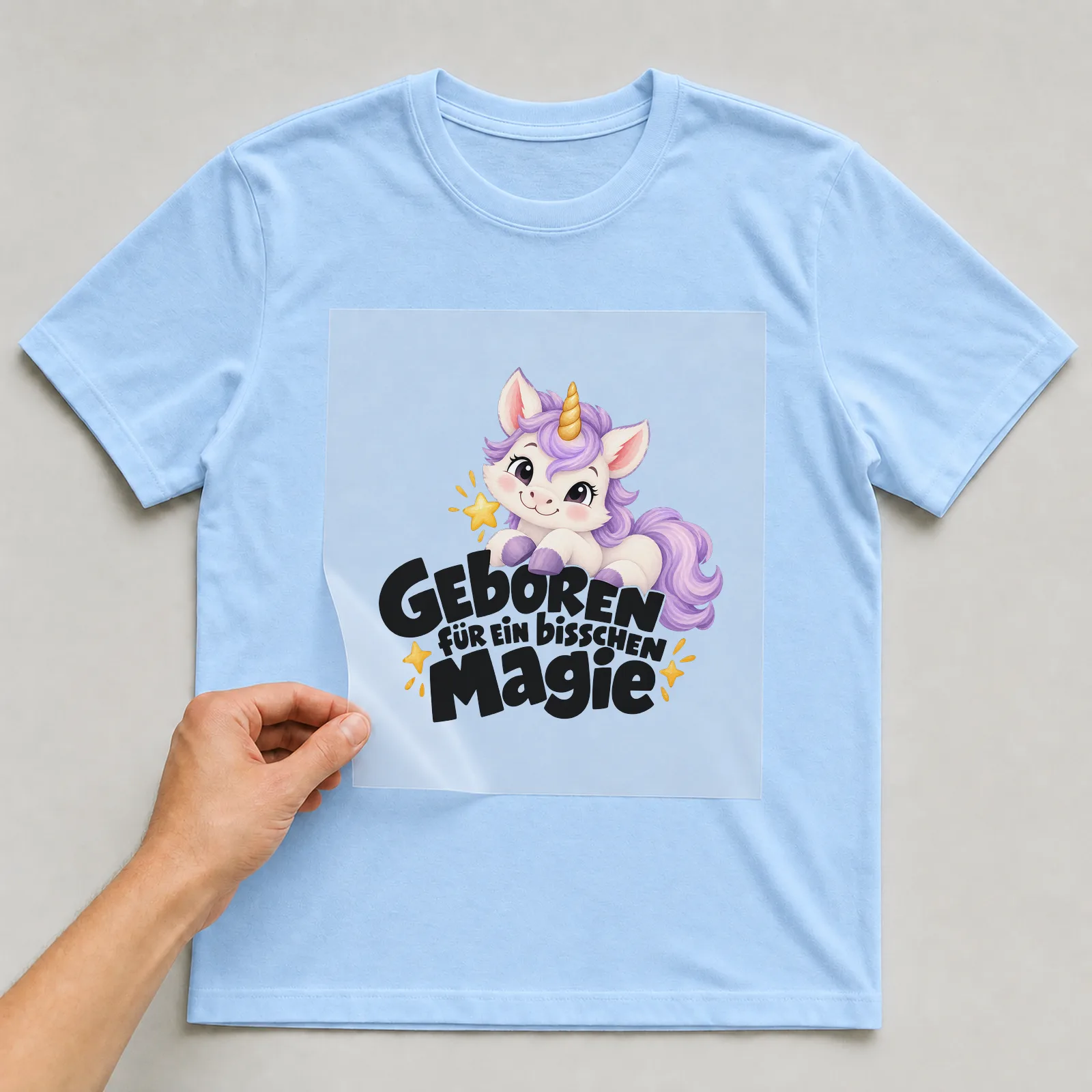 Bügelbild „Geboren für ein bisschen Magie“ auf hellblauem T-Shirt, Folie wird aufgelegt