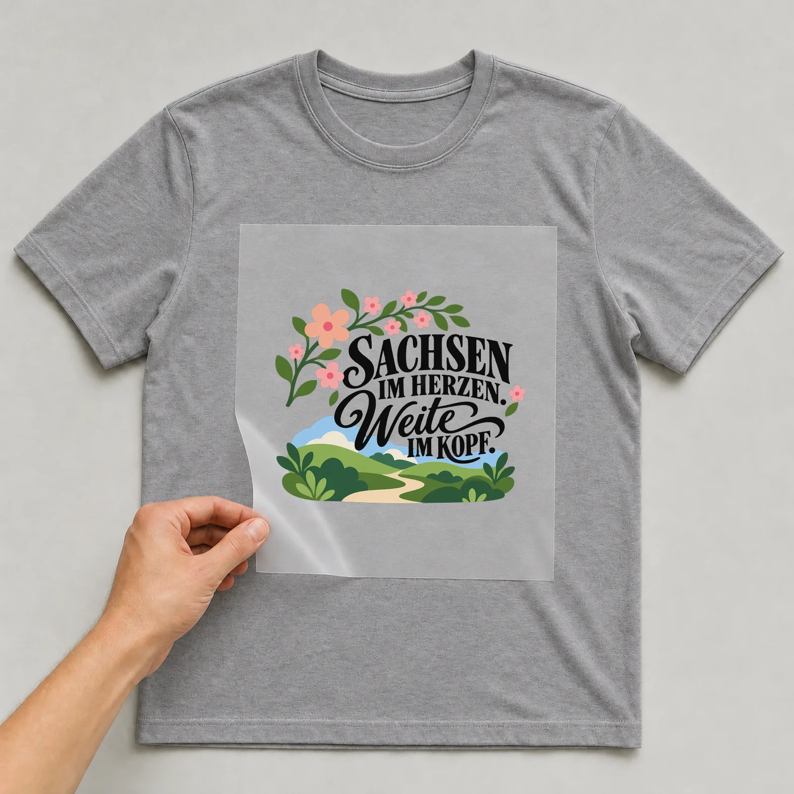 Bügelbild „SACHSEN IM HERZEN. Weite IM KOPF.“ auf grauem T-Shirt, Folie wird aufgelegt