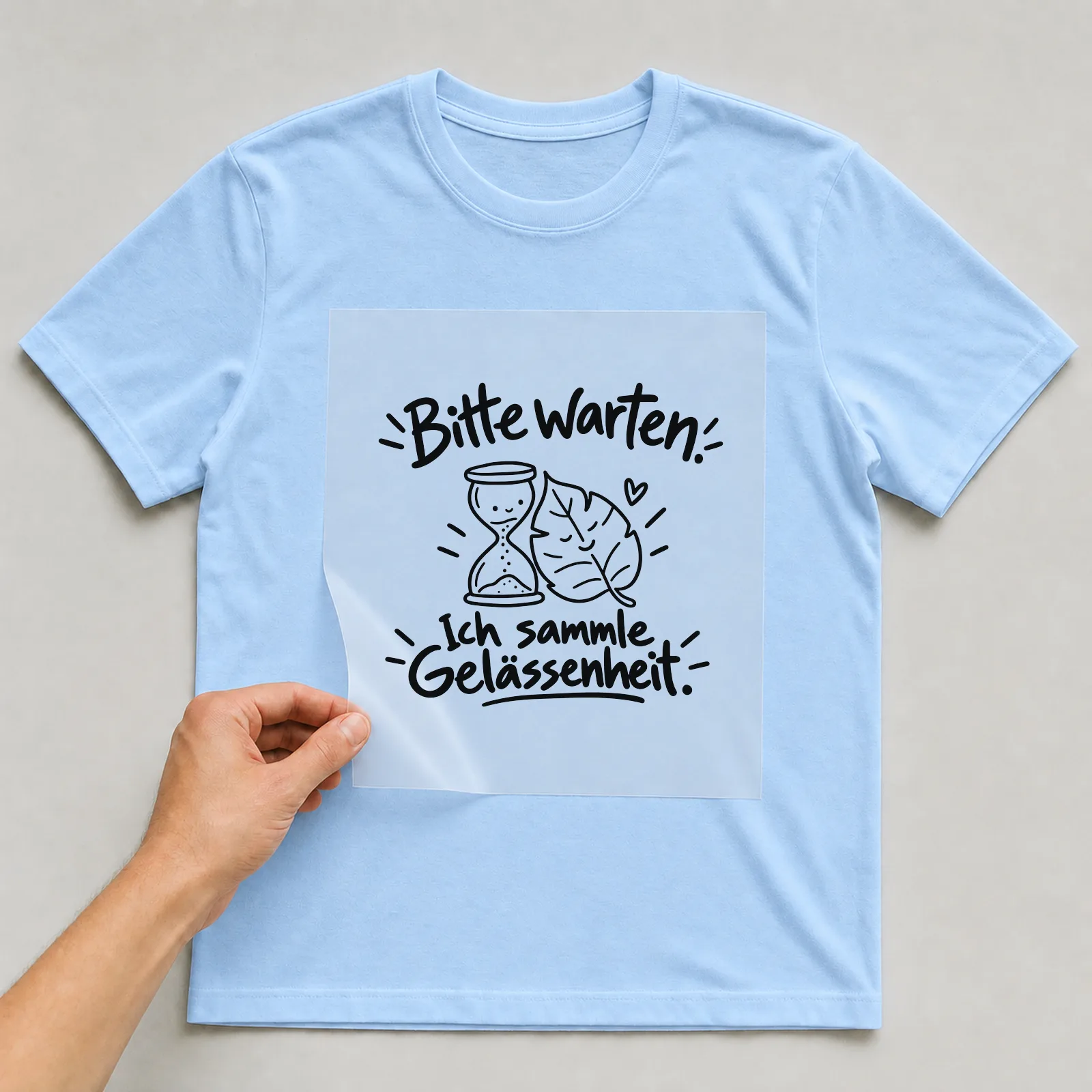 Bügelbild „Bitte warten. Ich sammle Gelassenheit.“ auf hellblauem T-Shirt, Folie wird aufgelegt