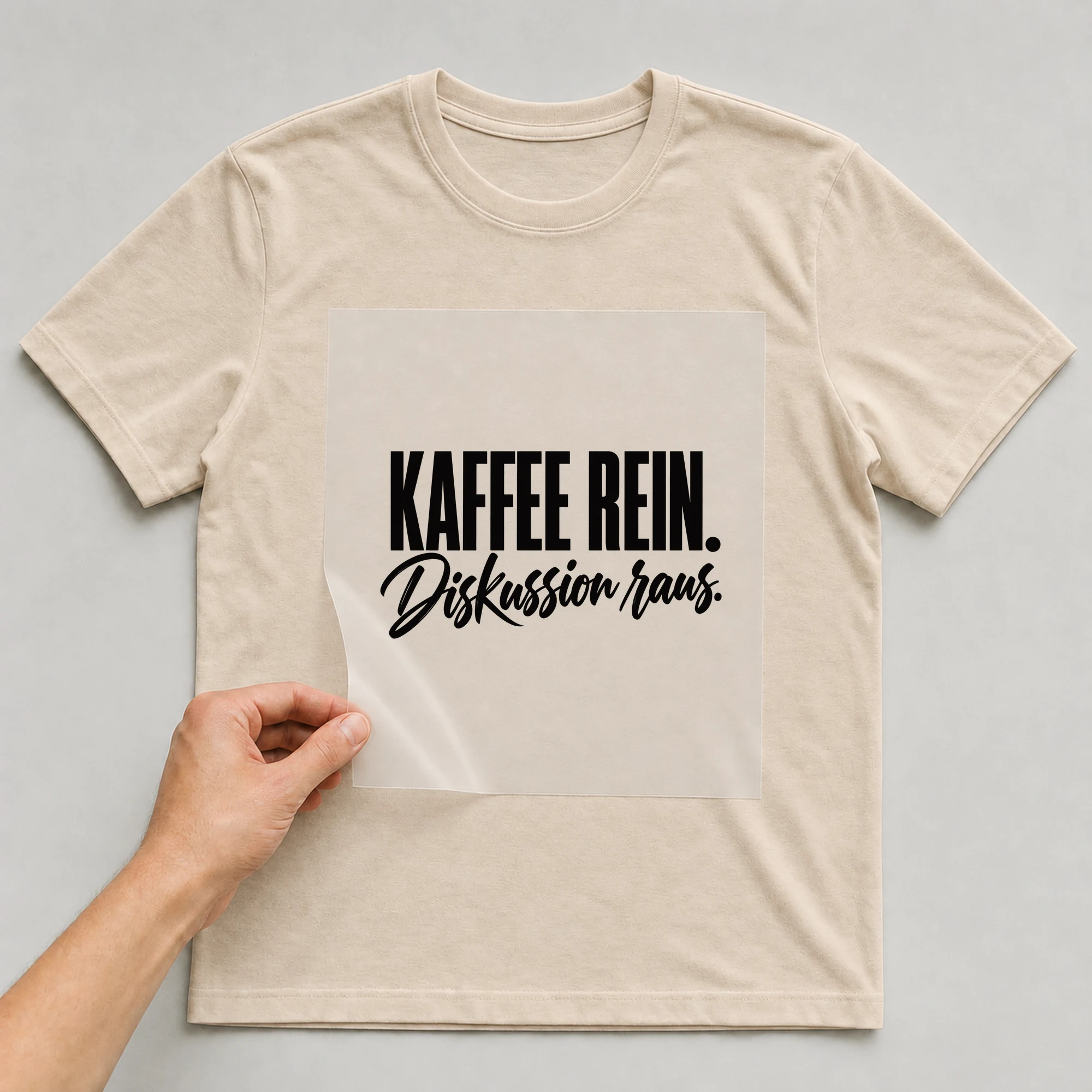 Bügelbild „Kaffee rein. Diskussion raus.“ auf babyblauem T-Shirt, Folie wird aufgelegt