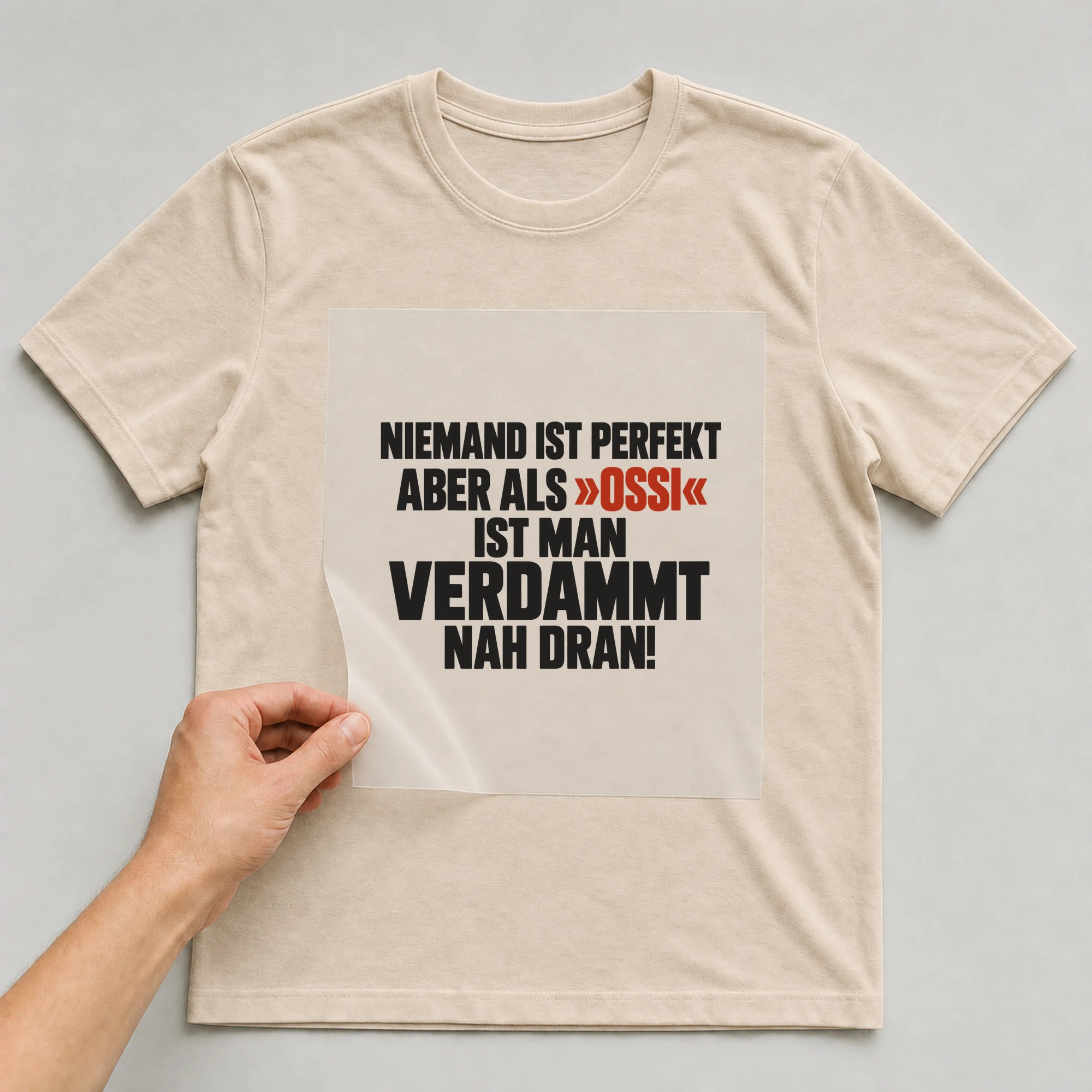 Bügelbild „Niemand ist perfekt aber als »Ossi« ist man verdammt nah dran!“ auf beigem T-Shirt, Folie wird aufgelegt