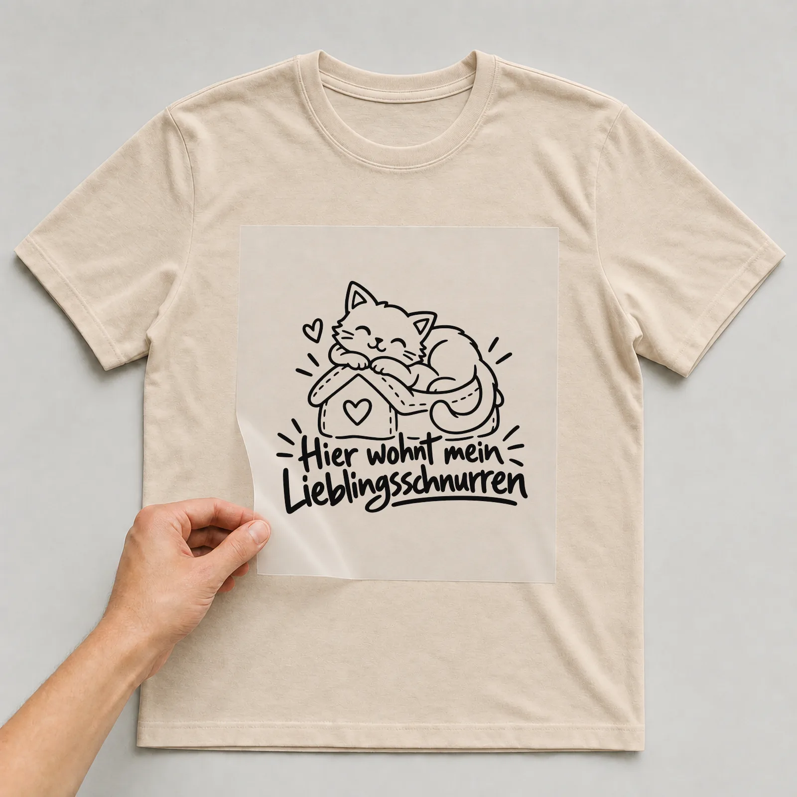 Bügelbild „Hier wohnt mein Lieblingsschnurren“ auf beigem T-Shirt, Folie wird aufgelegt