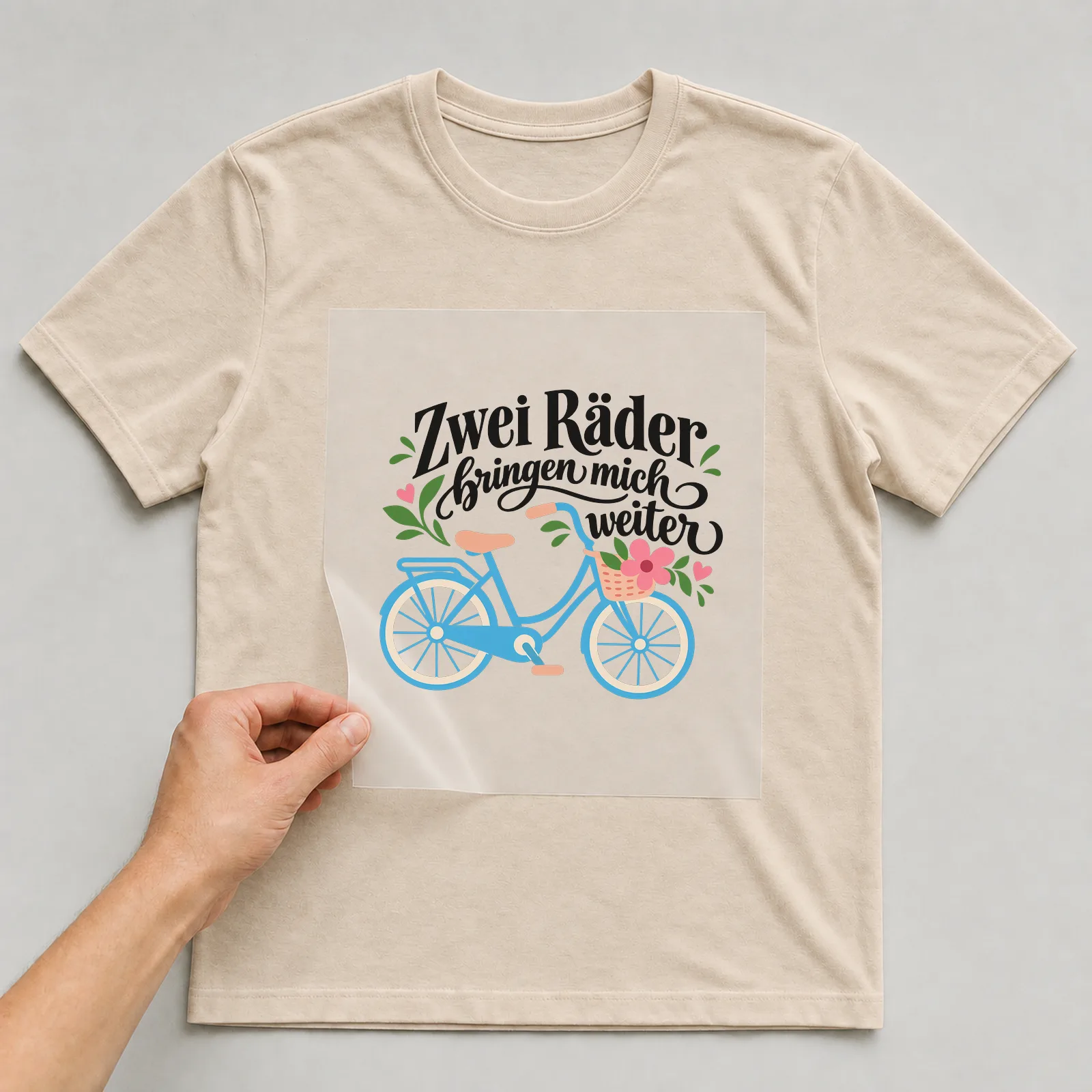 Bügelbild „Zwei Räder bringen mich weiter“ auf beigem T-Shirt, Folie wird aufgelegt