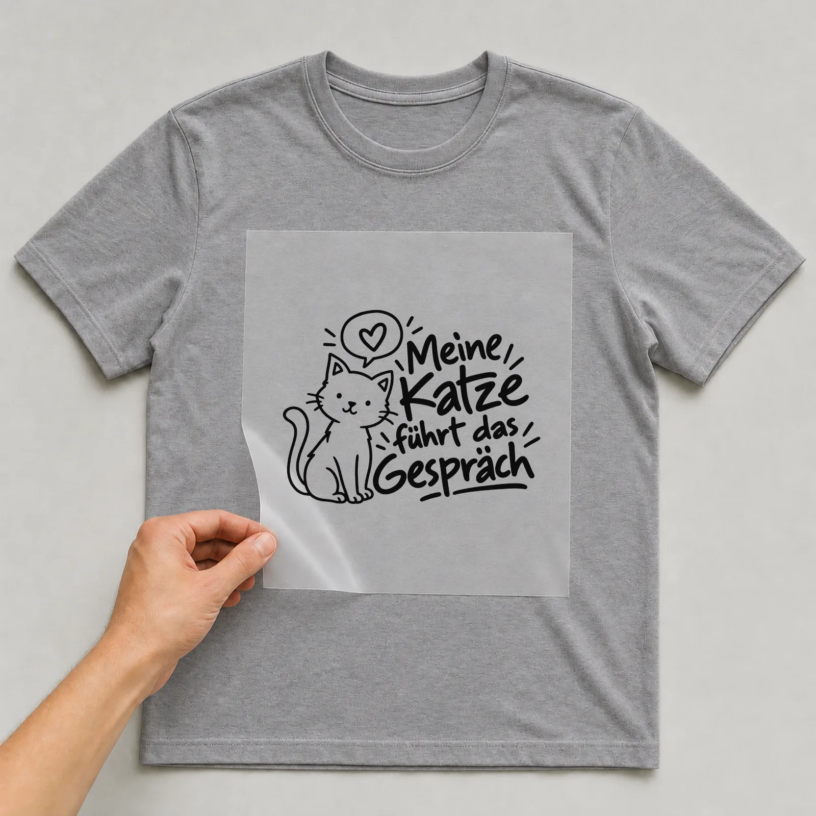 Bügelbild „Meine Katze führt das Gespräch“ auf grauem T-Shirt, Folie wird aufgelegt