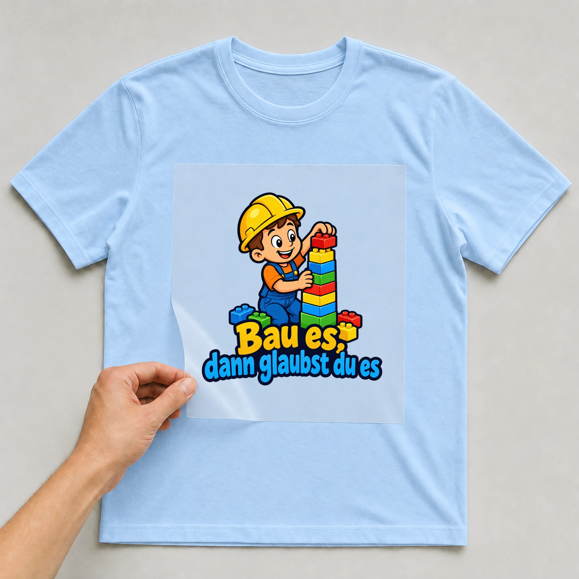 Bügelbild „Bau es, dann glaubst du es“ auf babyblauem T-Shirt, Folie wird aufgelegt