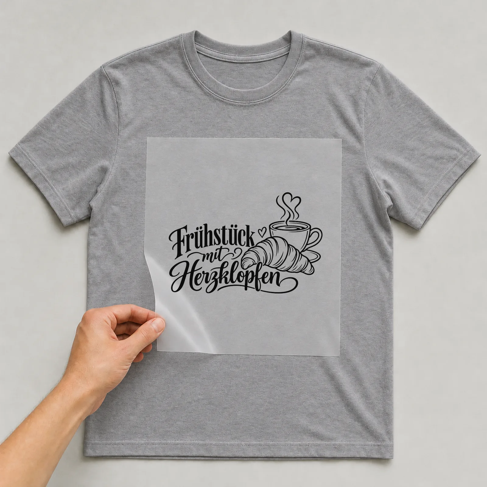 Bügelbild „Frühstück mit Herzklopfen“ auf grauem T-Shirt, Folie wird aufgelegt