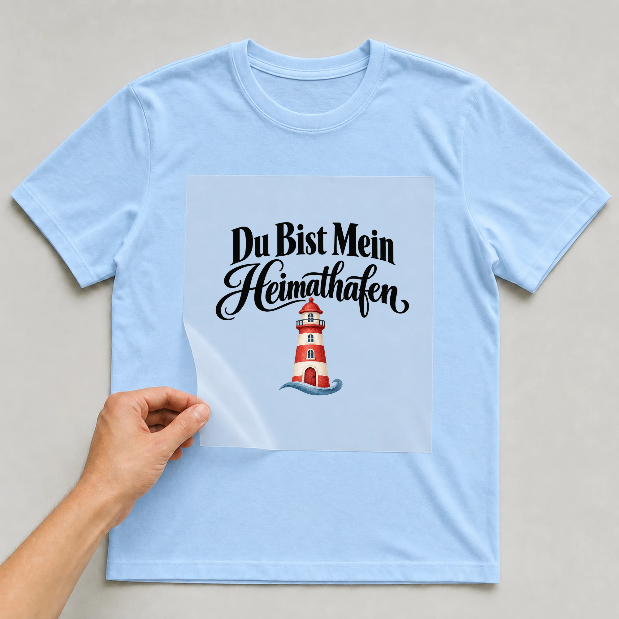 Bügelbild „Du bist mein Heimathafen“ auf babyblauem T-Shirt, Folie wird aufgelegt