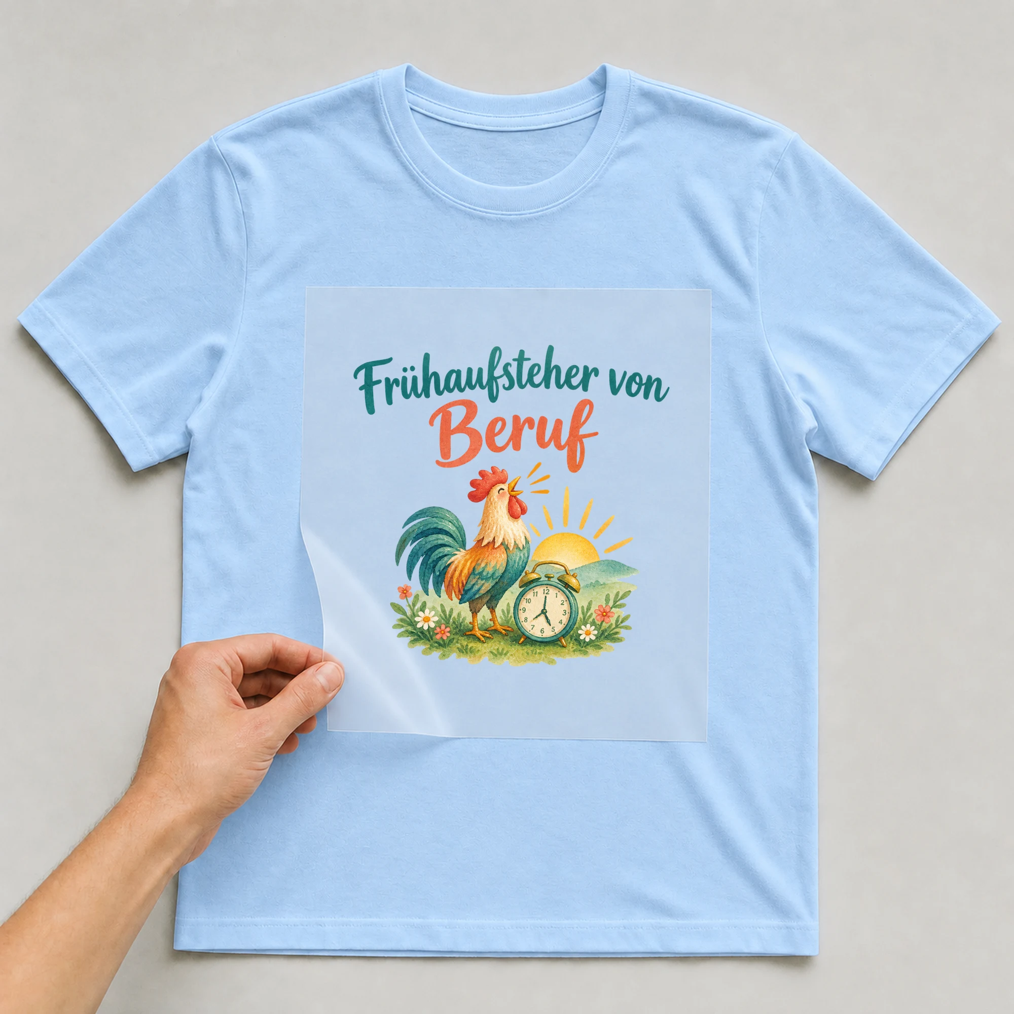 Bügelbild „Frühaufsteher von Beruf“ auf babyblauem T-Shirt, Folie wird aufgelegt