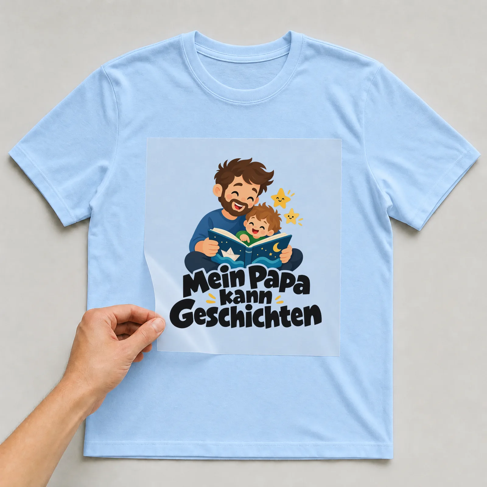 Bügelbild „Mein Papa kann Geschichten“ auf hellblauem T-Shirt, Folie wird aufgelegt