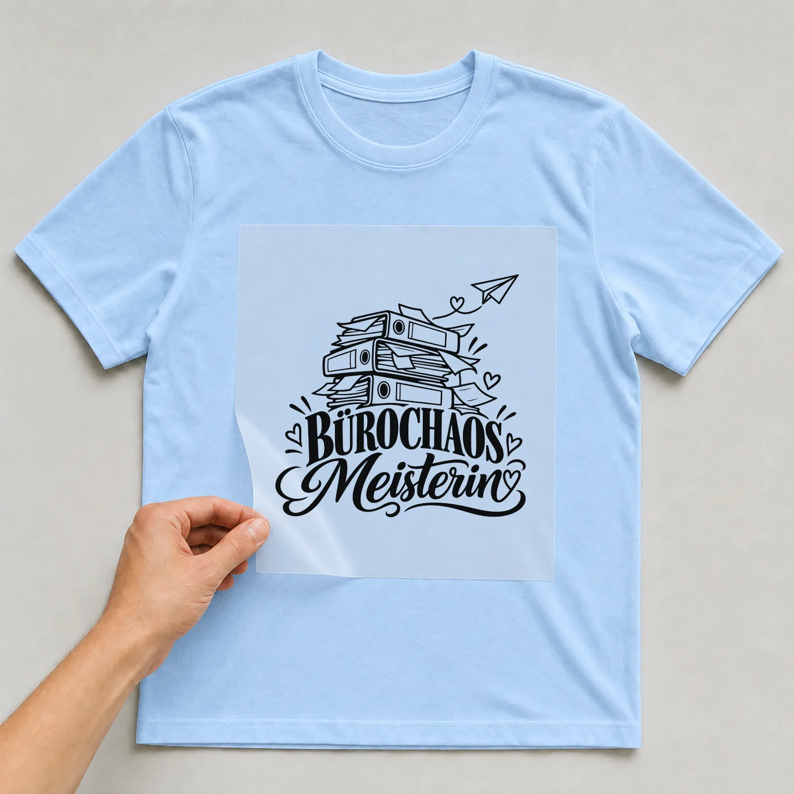 Bügelbild „Bürochaos Meisterin“ auf hellblauem T-Shirt, Folie wird aufgelegt