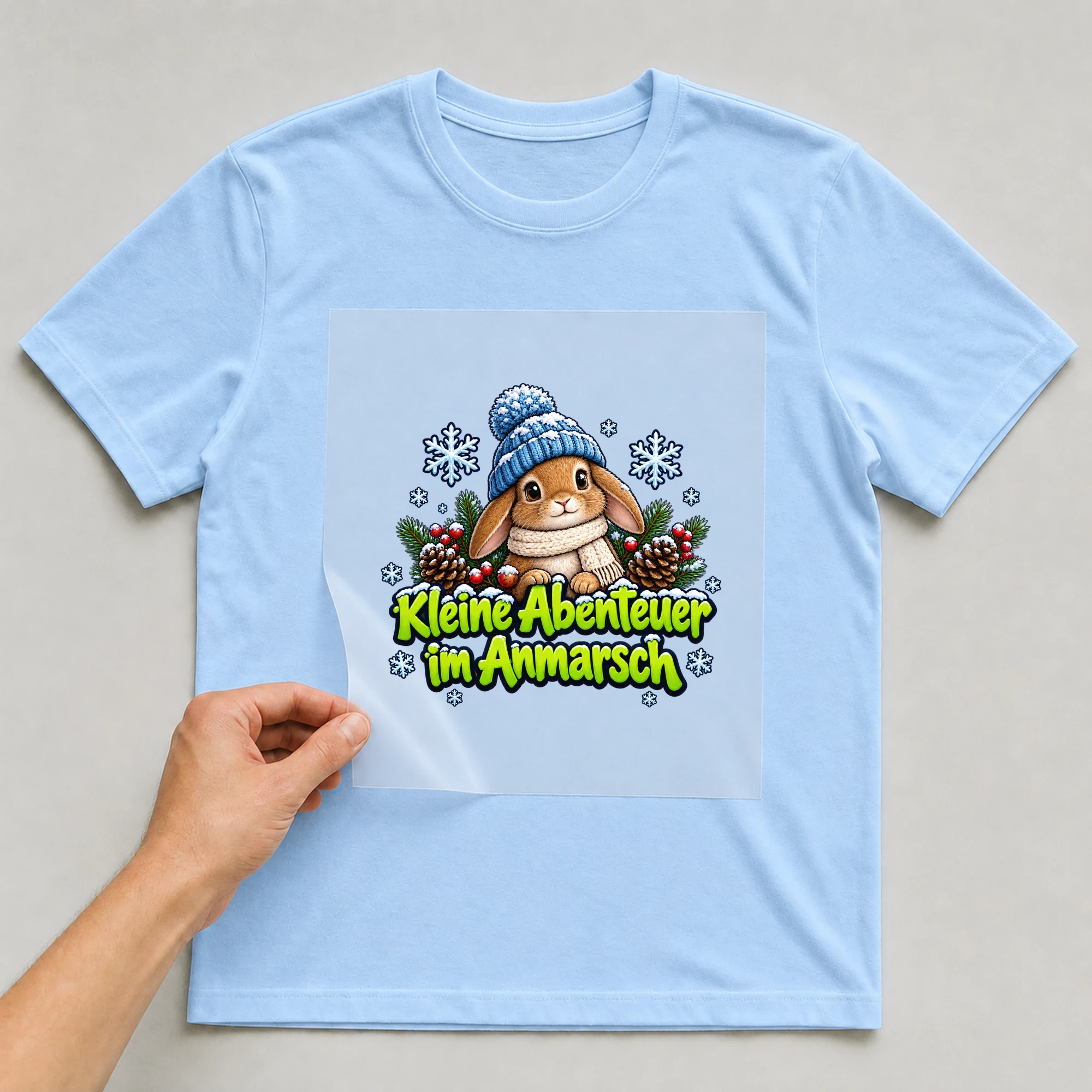 Bügelbild „Kleine Abenteuer im Anmarsch“ auf hellblauem T-Shirt, Folie wird aufgelegt