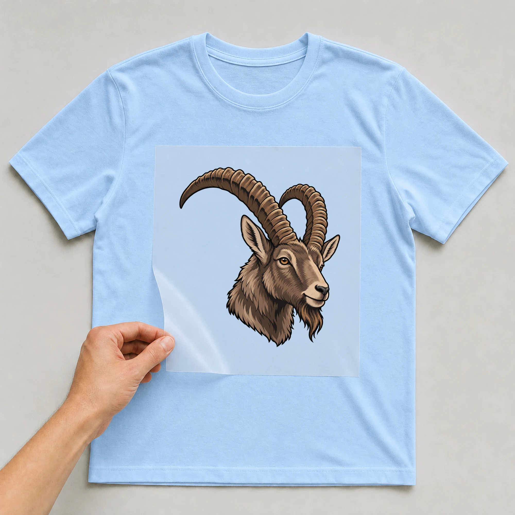 Bügelbild „Kritzel Stil Sternzeichen Steinbock“ auf babyblauem T-Shirt, Folie wird aufgelegt