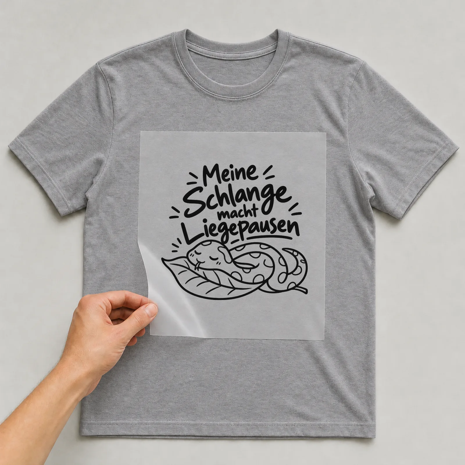 Bügelbild „Meine Schlange macht Liegepausen“ auf grauem T-Shirt, Folie wird aufgelegt