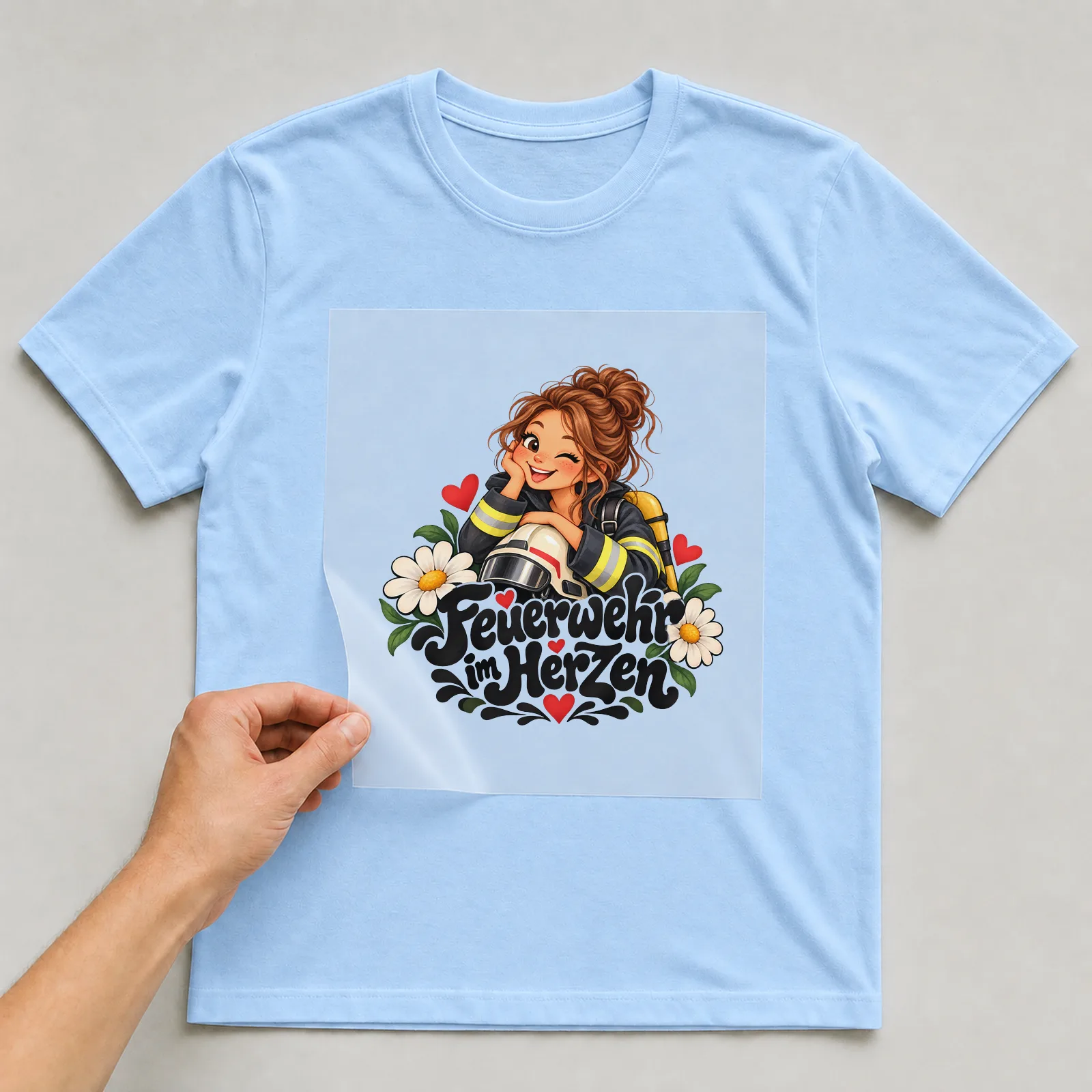 Bügelbild „Feuerwehr im Herzen“ auf hellblauem T-Shirt, Folie wird aufgelegt