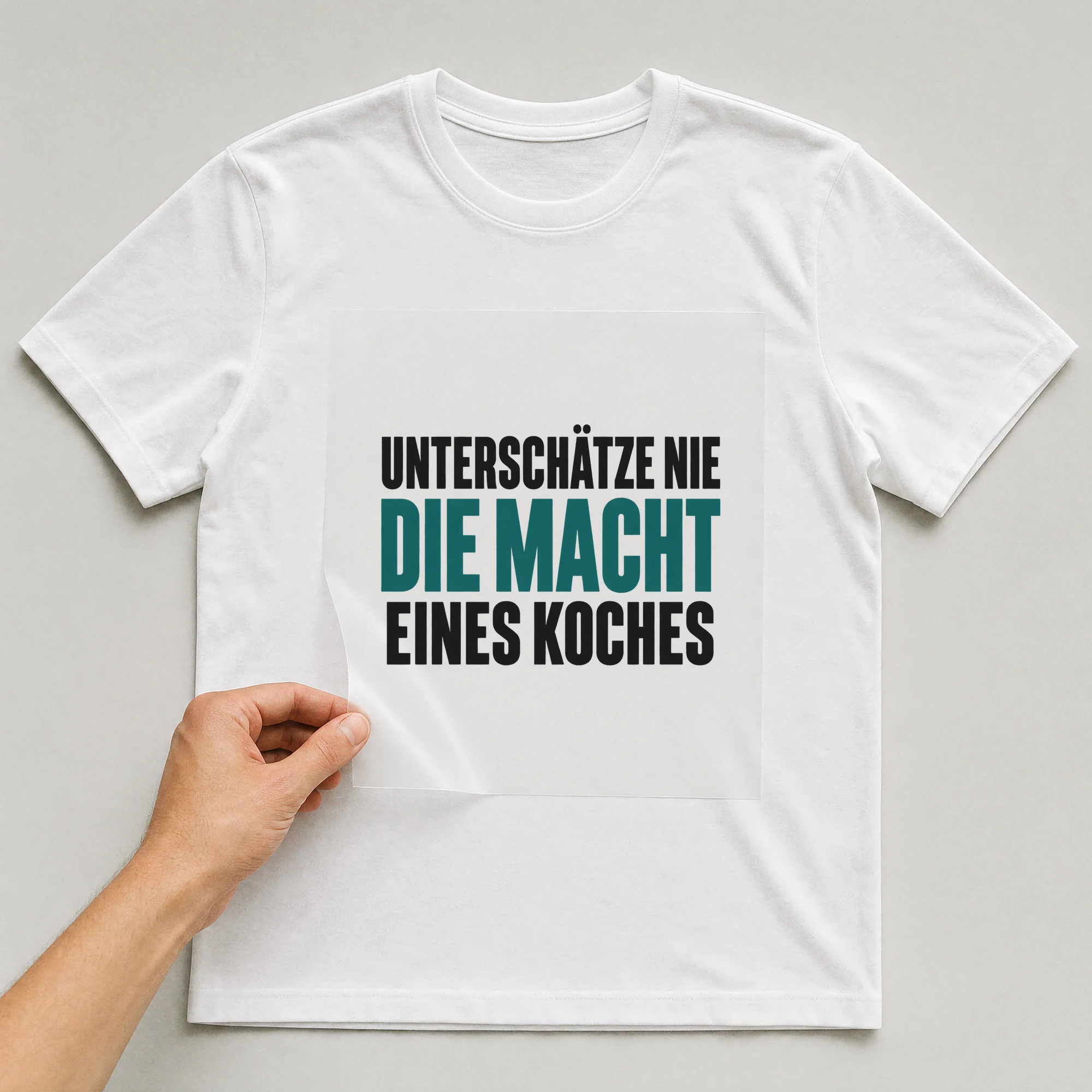 Bügelbild „Unterschätze nie die macht eines Koches“ auf weißem T-Shirt, Folie wird aufgelegt