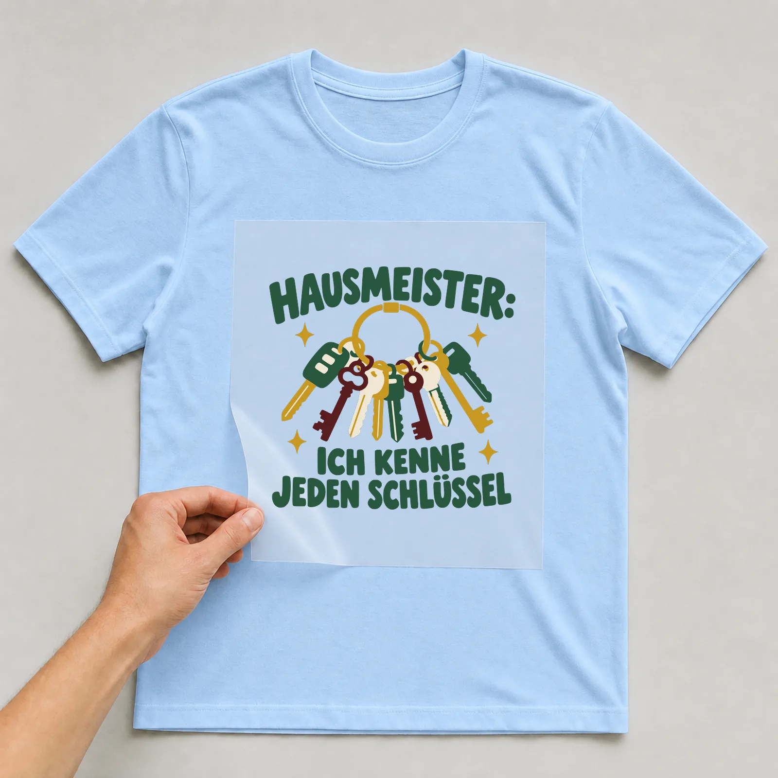 Bügelbild Hausmeister: Ich kenne jeden Schlüssel auf hellblauem T-Shirt, Folie wird aufgelegt