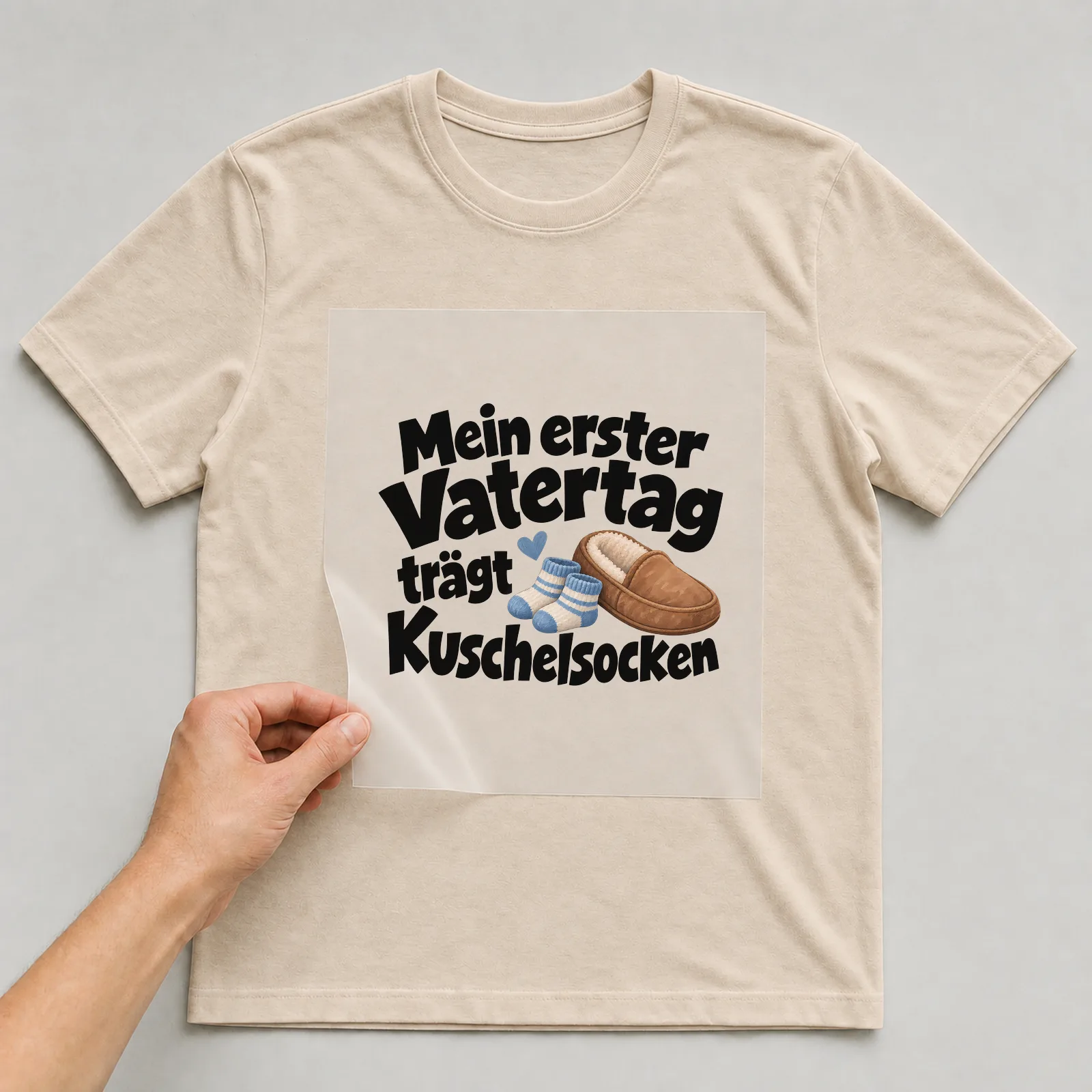 Bügelbild „Mein erster Vatertag trägt Kuschelsocken“ auf beigem T-Shirt, Folie wird aufgelegt