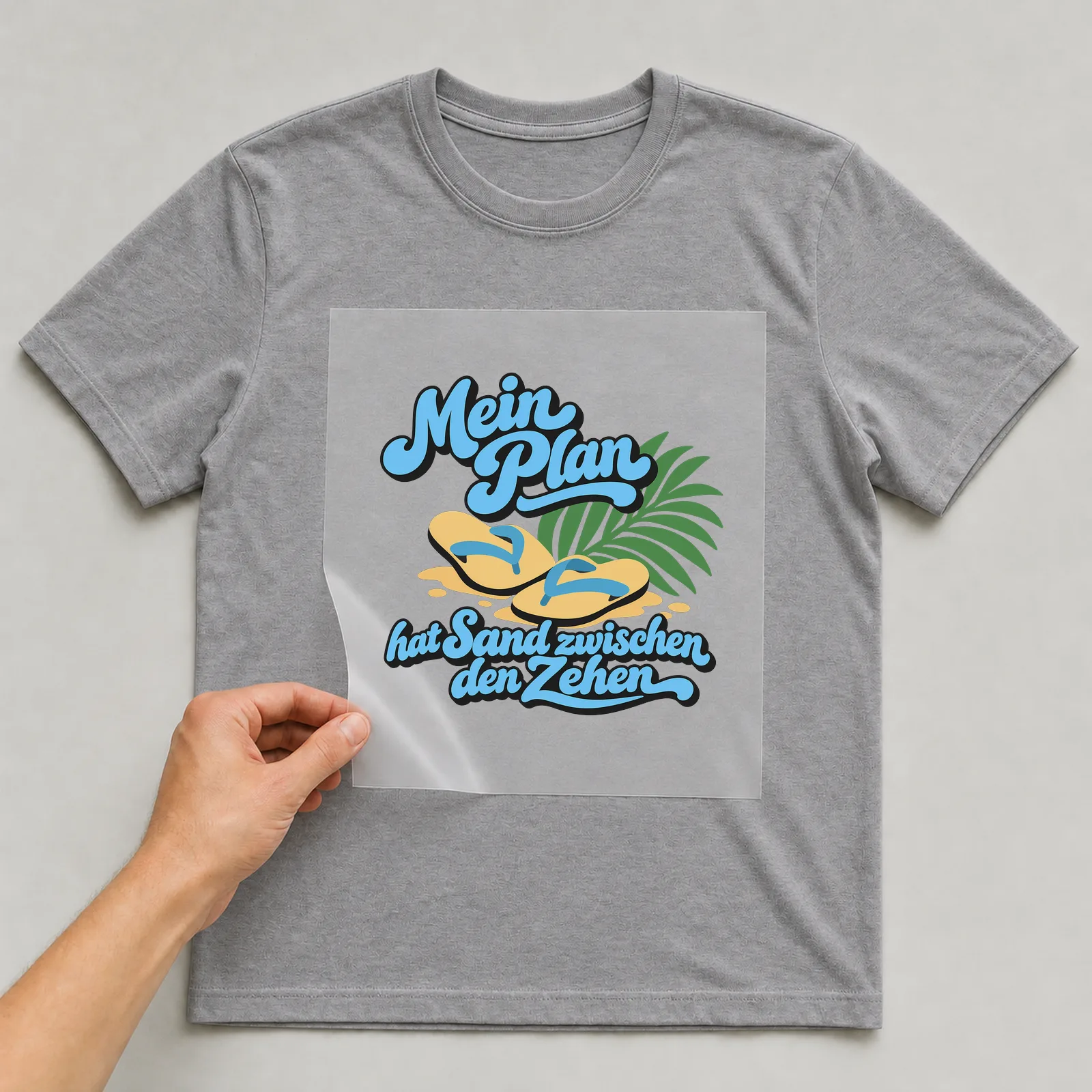 Bügelbild „Mein Plan hat Sand zwischen den Zehen“ auf grauem T-Shirt, Folie wird aufgelegt