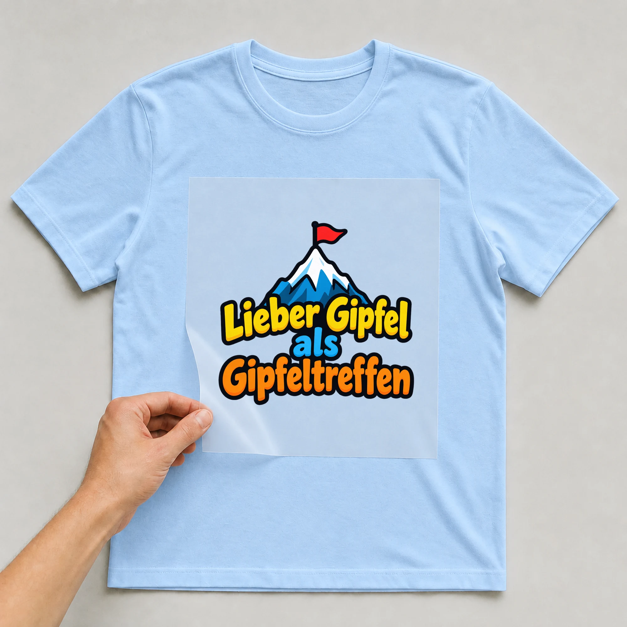 Bügelbild „Lieber gipfel als gipfeltreffen“ auf babyblauem T-Shirt, Folie wird aufgelegt
