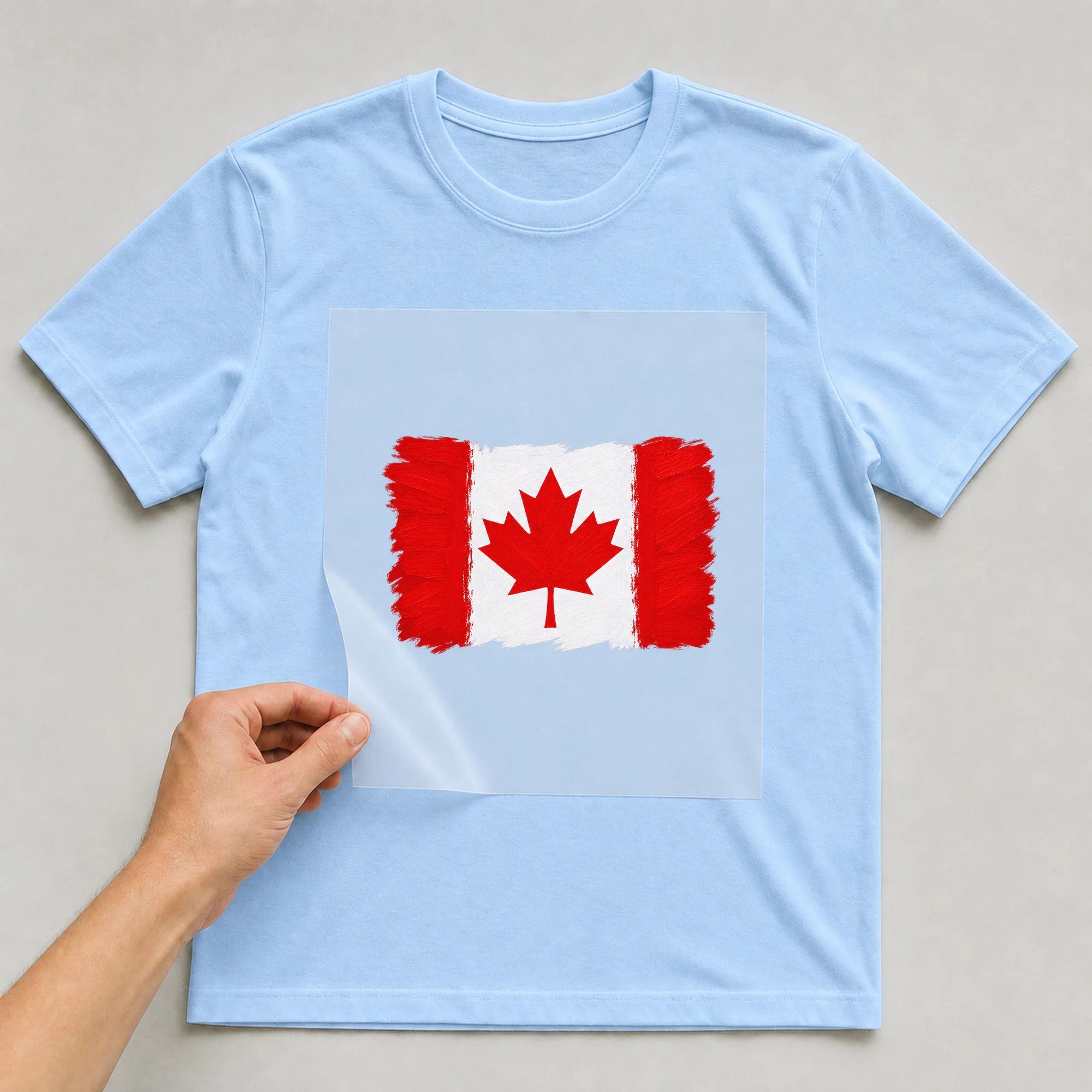 Bügelbild „Flagge Kanada im Pinselstrich“ auf babyblauem T-Shirt, Folie wird aufgelegt