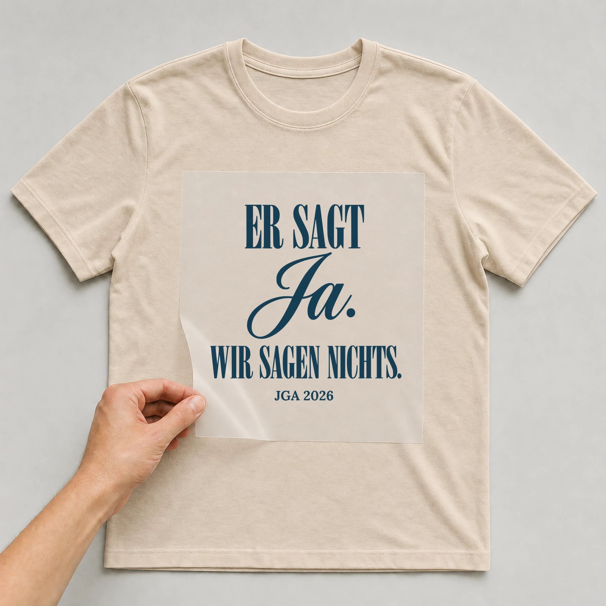 Bügelbild Er sagt Ja. Wir sagen nichts. auf beigem T-Shirt, Folie wird aufgelegt