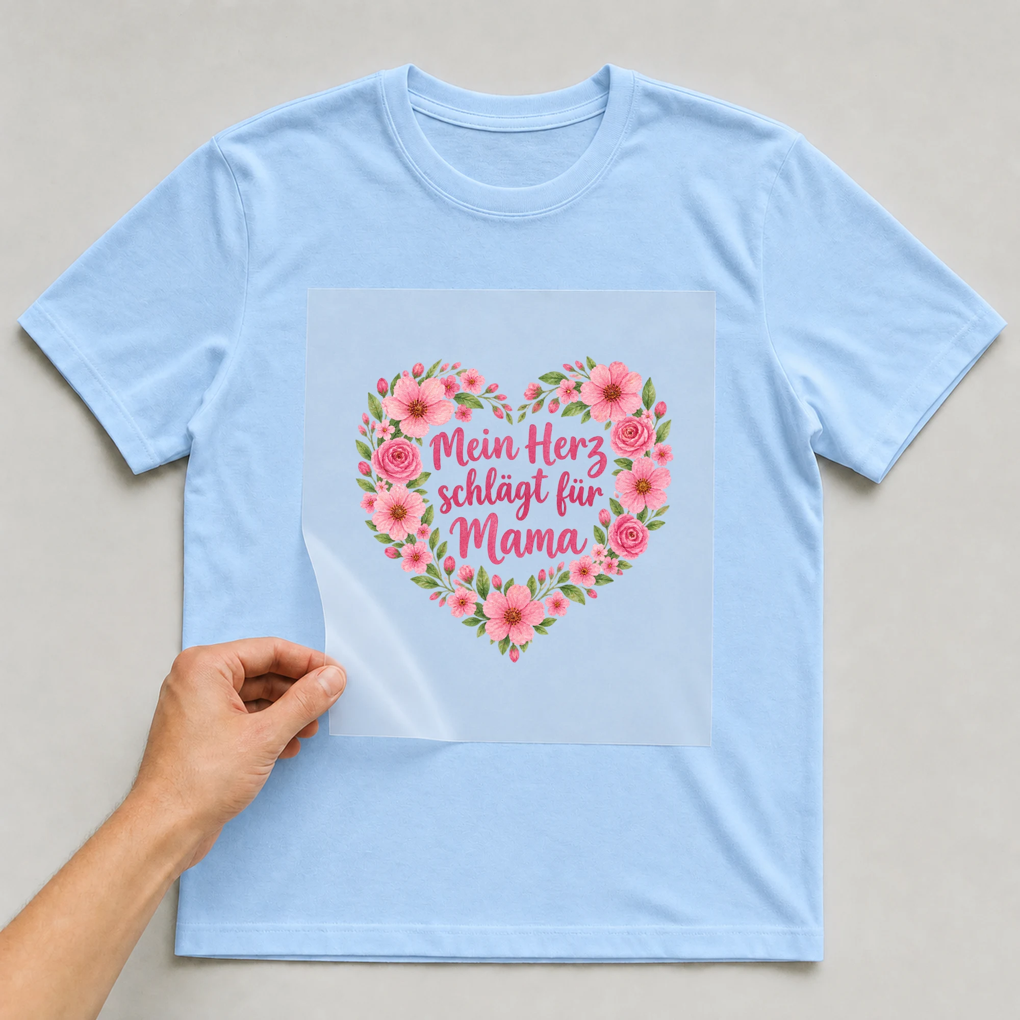 Bügelbild „Mein Herz schlägt für Mama“ auf babyblauem T-Shirt, Folie wird aufgelegt