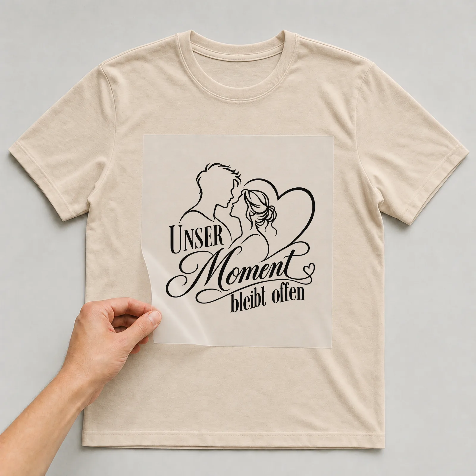 Bügelbild „Unser Moment bleibt offen“ auf beigem T-Shirt, Folie wird aufgelegt