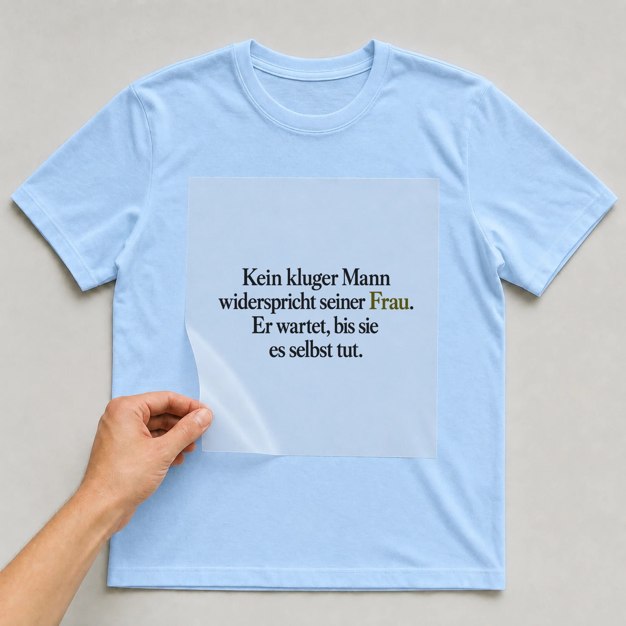 Bügelbild „Kein kluger Mann widerspricht seiner Frau. Er wartet, bis sie es selbst tut.“ auf babyblauem T-Shirt, Folie wird aufgelegt