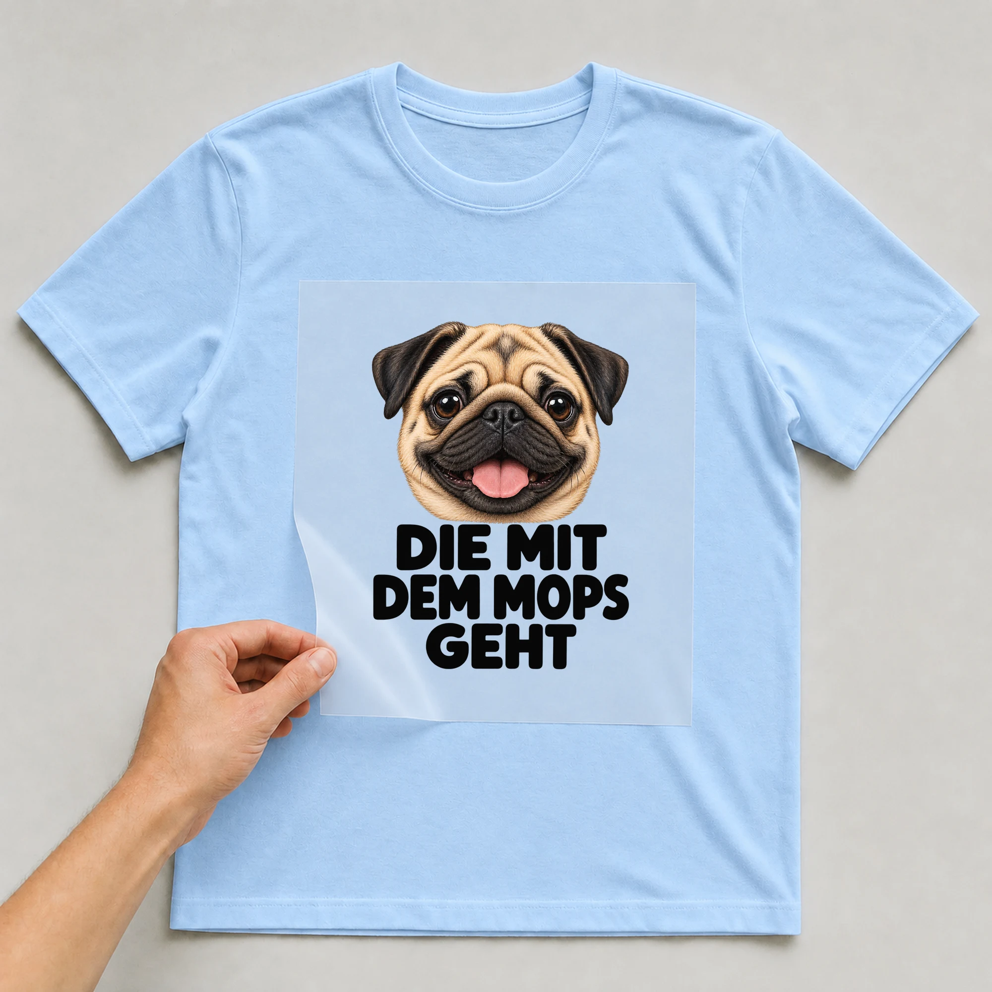Bügelbild „Die mit dem Mops geht“ auf babyblauem T-Shirt, Folie wird aufgelegt