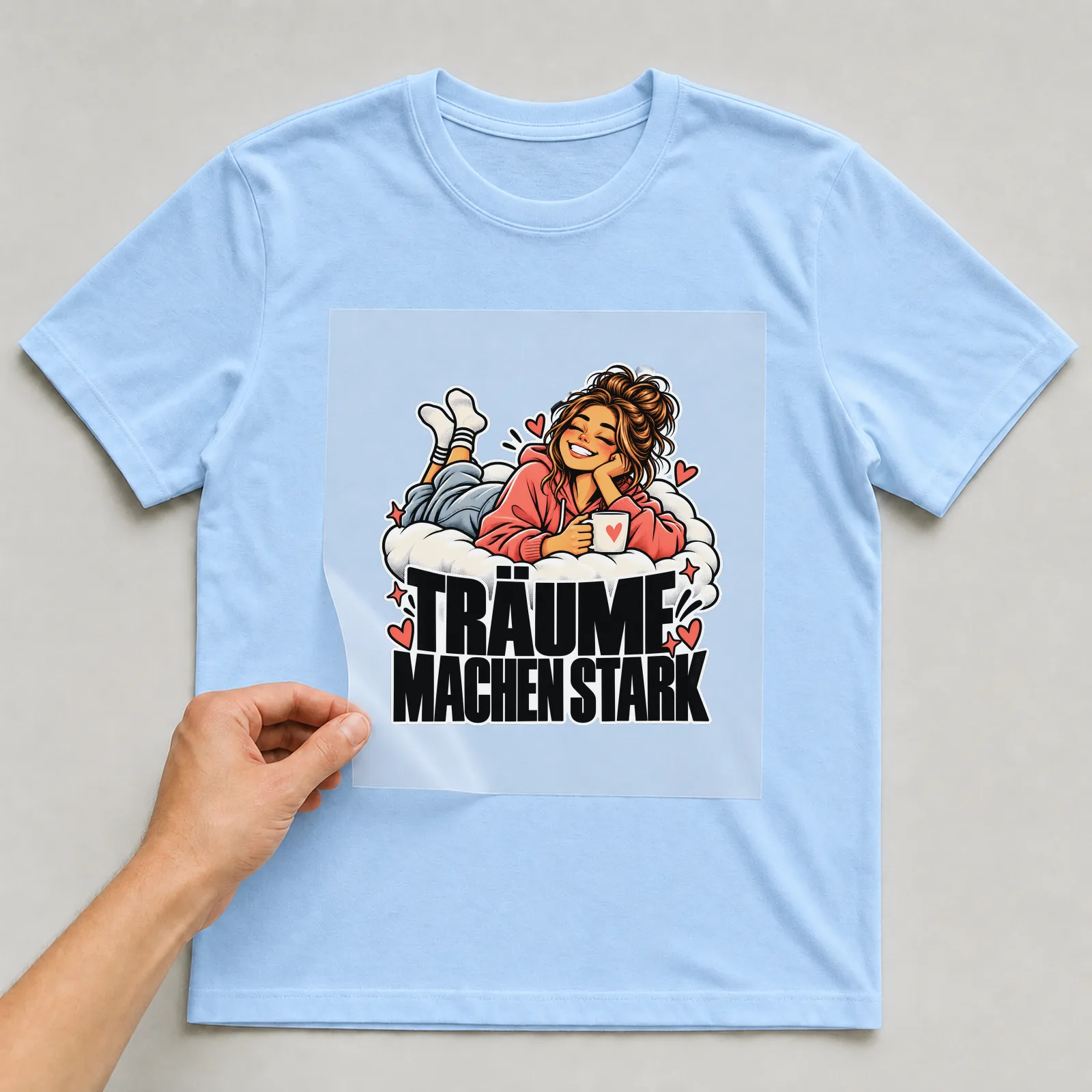 Bügelbild „Träume machen stark“ auf hellblauem T-Shirt, Folie wird aufgelegt