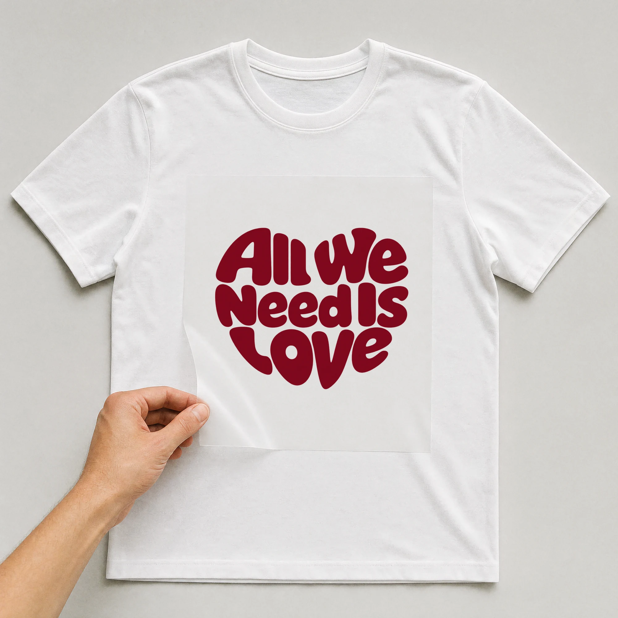 Bügelbild „All We Need Is Love“ auf weißem T-Shirt, Folie wird aufgelegt