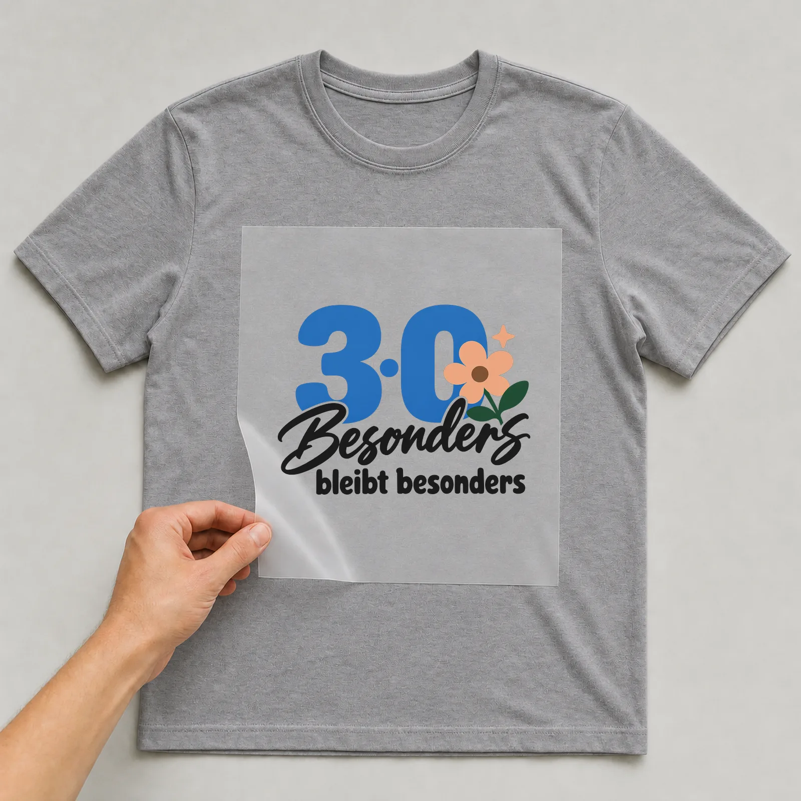 Bügelbild „30 · Besonders bleibt besonders“ auf grauem T-Shirt, Folie wird aufgelegt