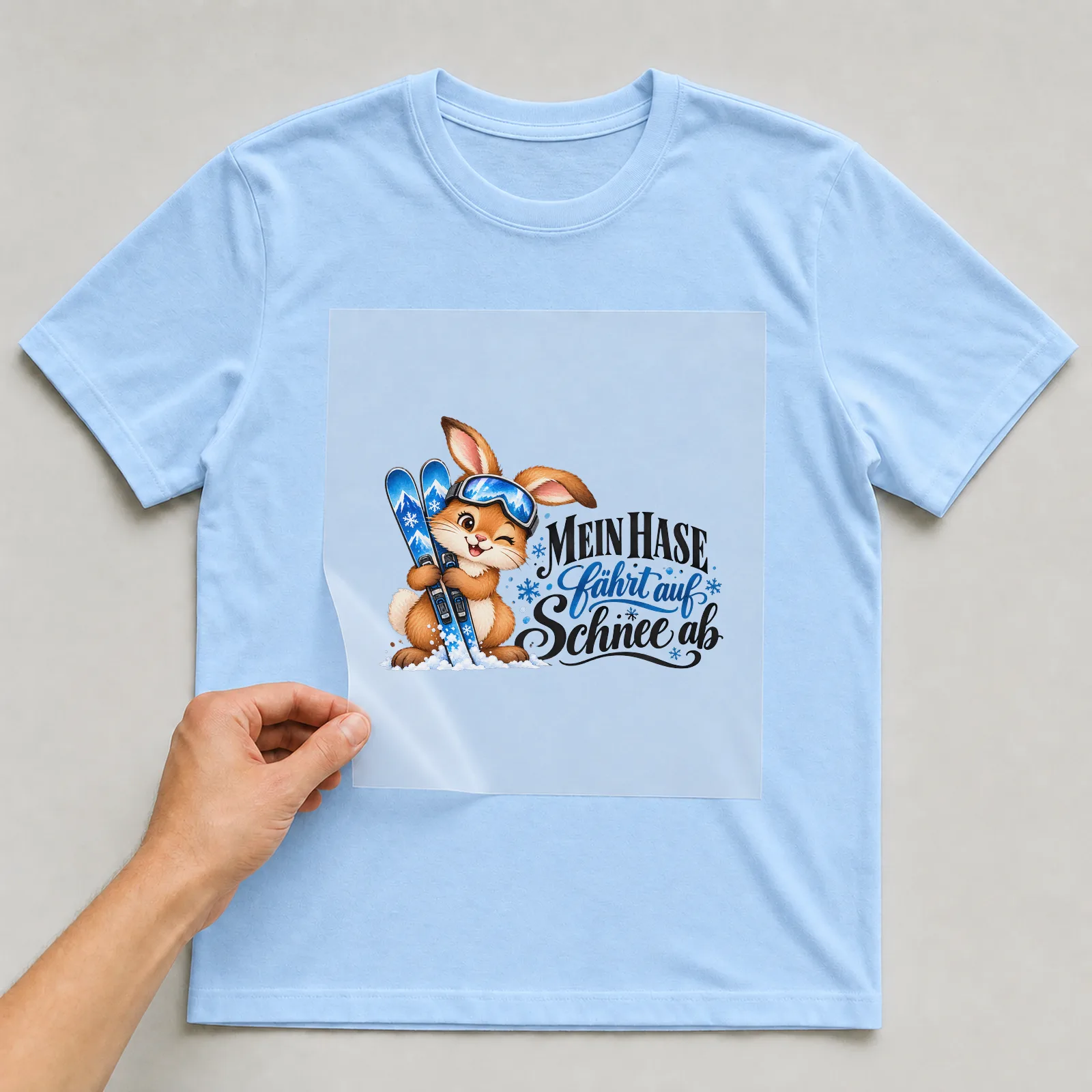 Bügelbild „Mein Hase fährt auf Schnee ab“ auf hellblauem T-Shirt, Folie wird aufgelegt